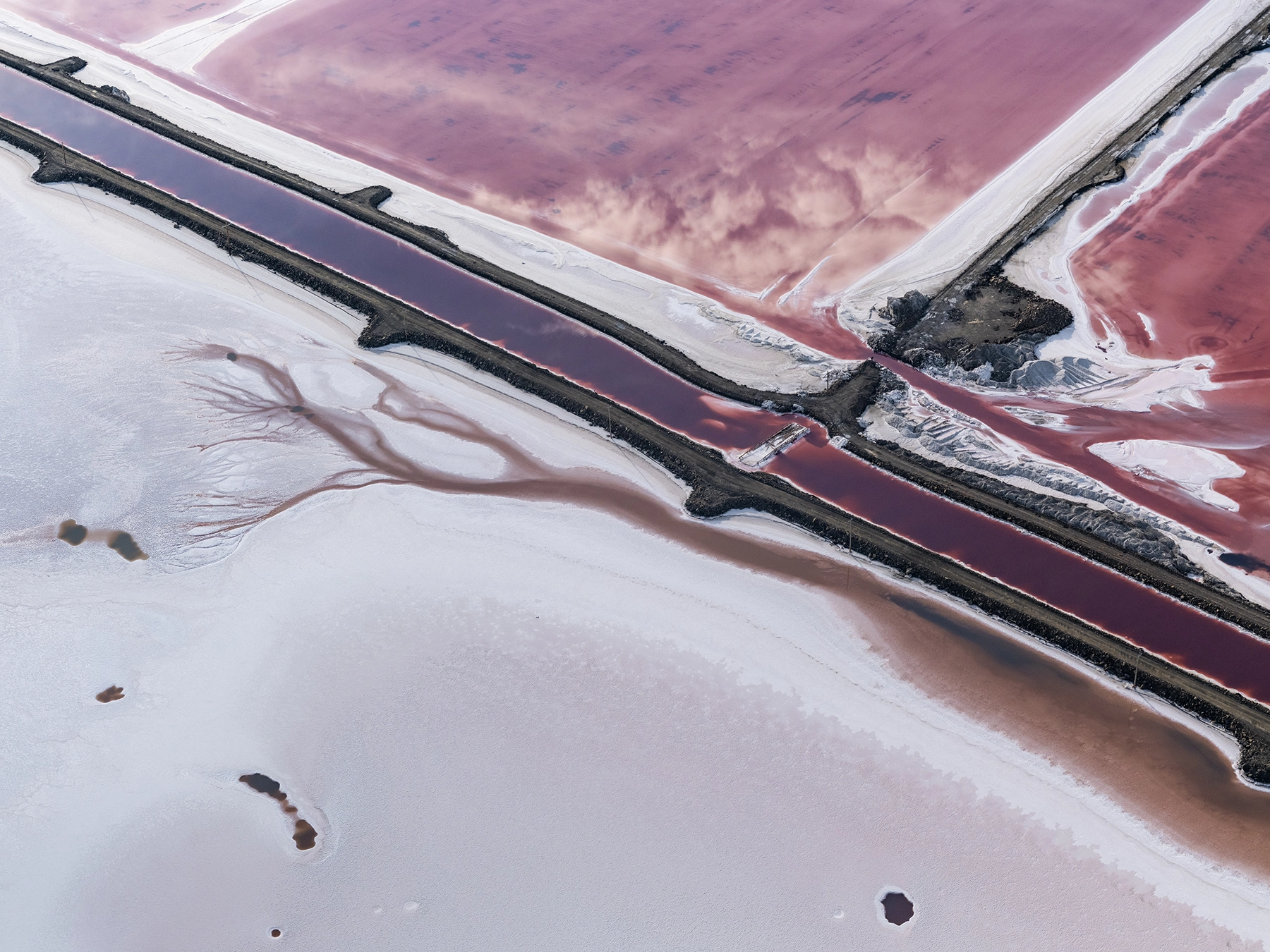 Aerial view of Compass Minerals solar evaporation ponds at the Great Salt Lake, showing geometric patterns of colorful mineral extraction ponds, levees, and industrial infrastructure impacting the lake's ecology.