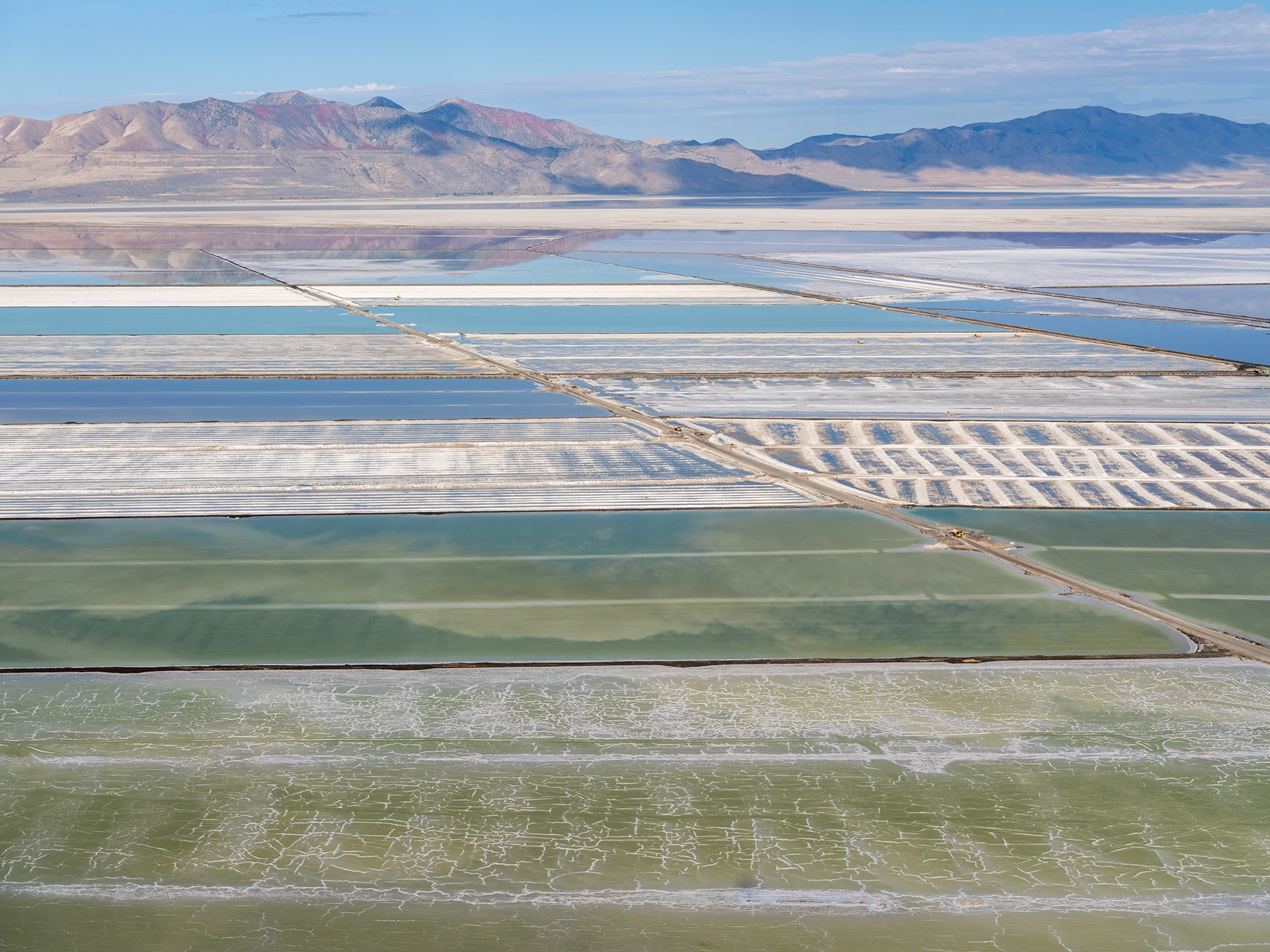Aerial view of Compass Minerals solar evaporation ponds at the Great Salt Lake, showing geometric patterns of colorful mineral extraction ponds, levees, and industrial infrastructure impacting the lake's ecology.