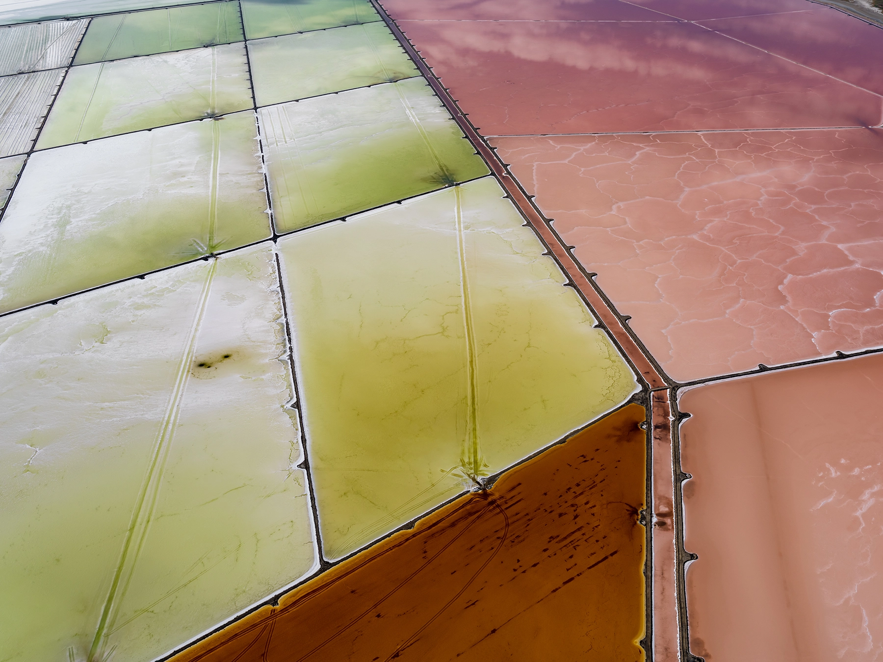 Aerial view of Compass Minerals solar evaporation ponds at the Great Salt Lake, showing geometric patterns of colorful mineral extraction ponds, levees, and industrial infrastructure impacting the lake's ecology.