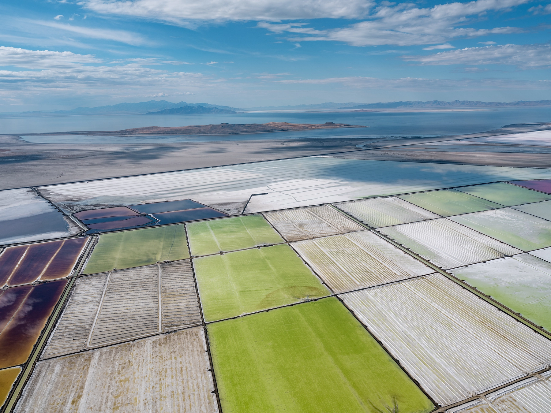 Aerial view of Compass Minerals solar evaporation ponds at the Great Salt Lake, showing geometric patterns of colorful mineral extraction ponds, levees, and industrial infrastructure impacting the lake's ecology.