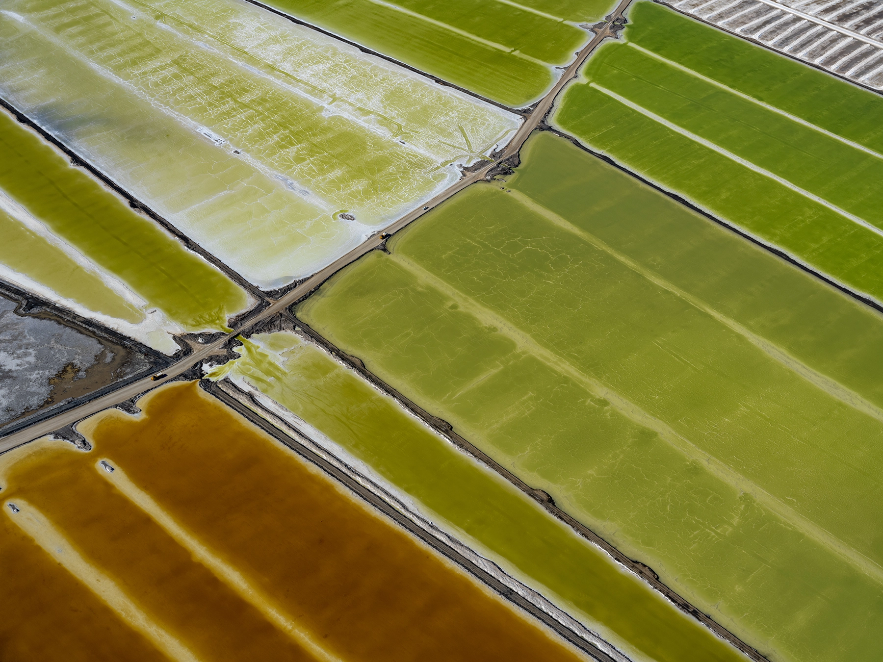 Aerial view of Compass Minerals solar evaporation ponds at the Great Salt Lake, showing geometric patterns of colorful mineral extraction ponds, levees, and industrial infrastructure impacting the lake's ecology.