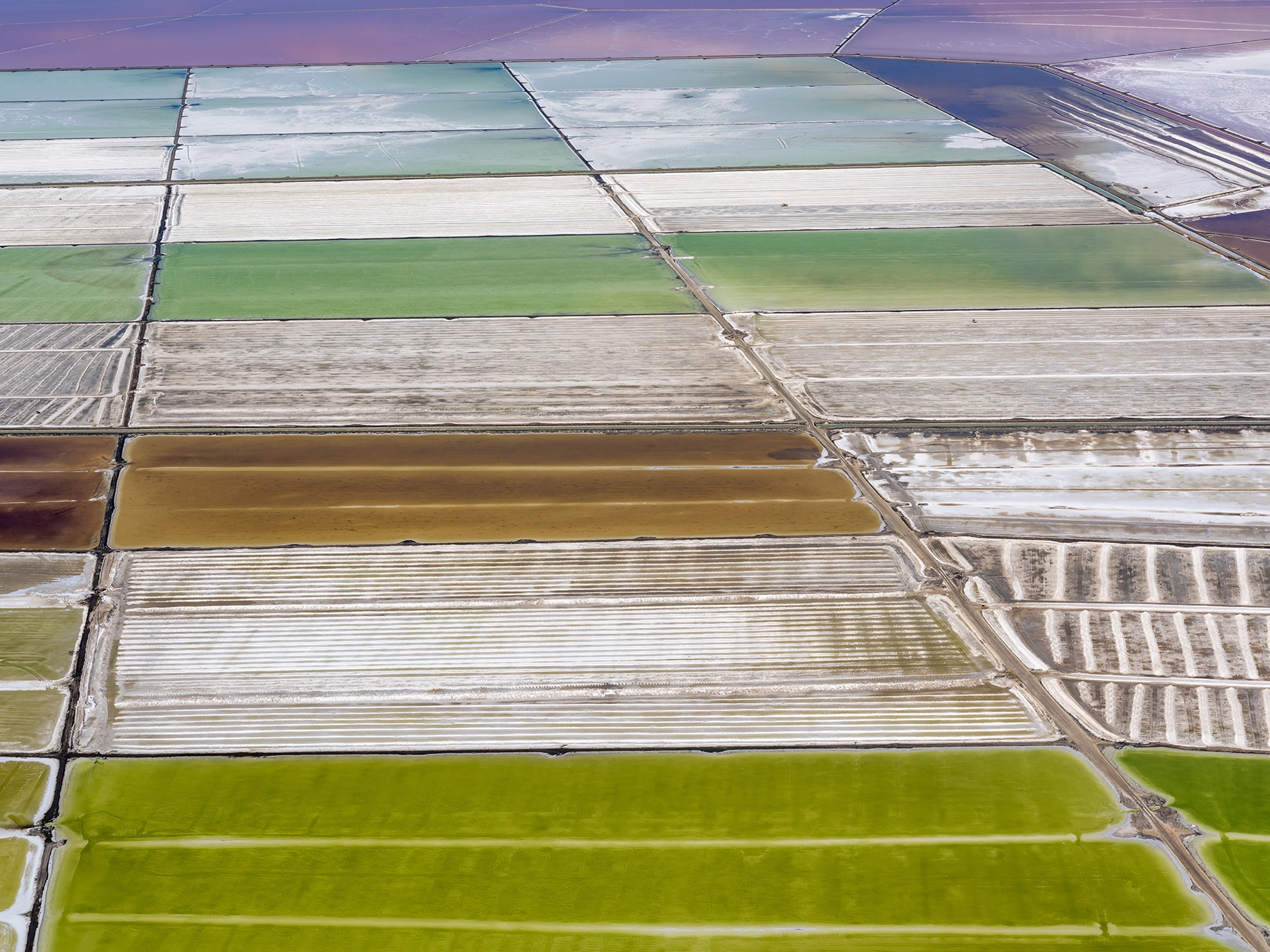 Aerial view of Compass Minerals solar evaporation ponds at the Great Salt Lake, showing geometric patterns of colorful mineral extraction ponds, levees, and industrial infrastructure impacting the lake's ecology.