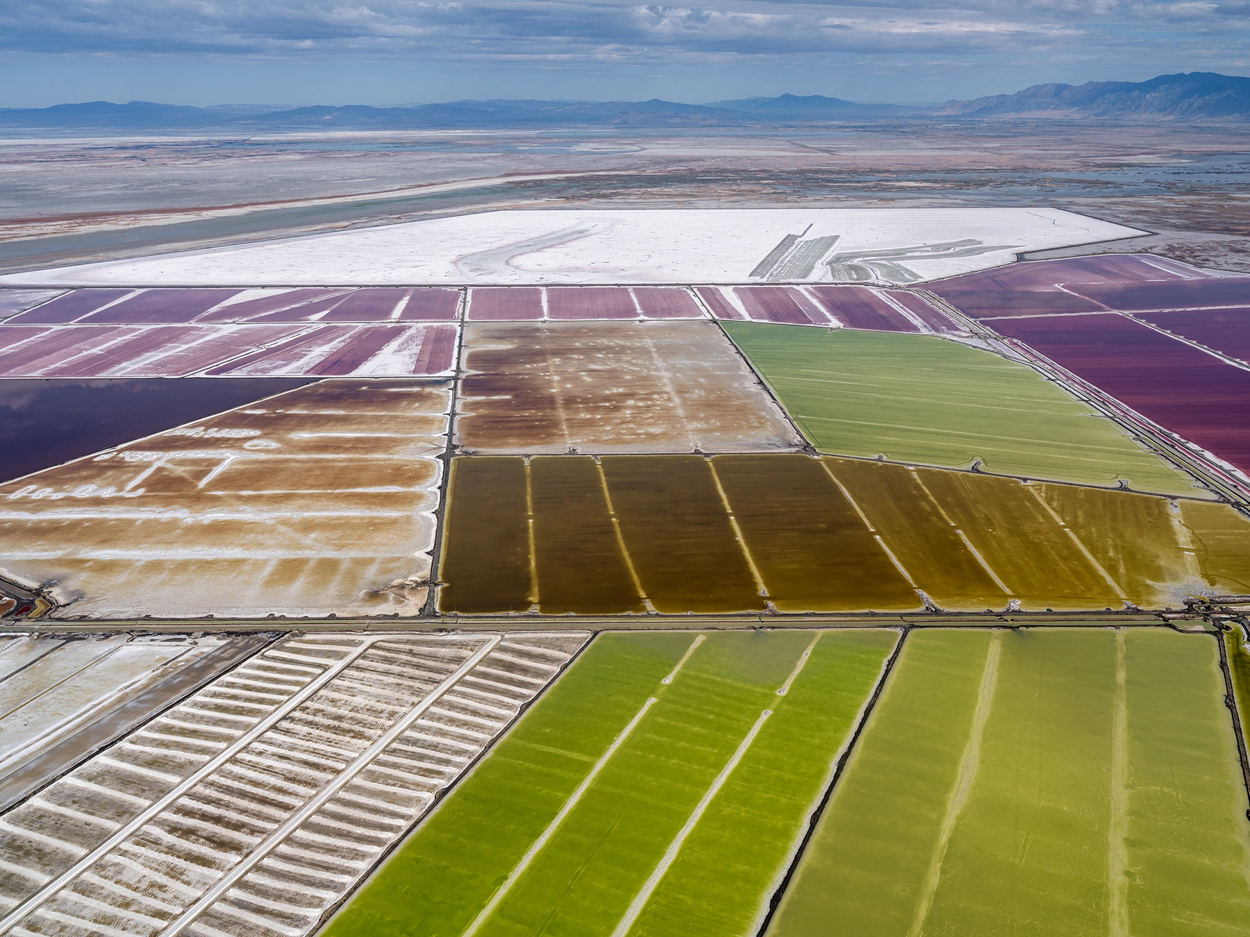Aerial view of Compass Minerals solar evaporation ponds at the Great Salt Lake, showing geometric patterns of colorful mineral extraction ponds, levees, and industrial infrastructure impacting the lake's ecology.