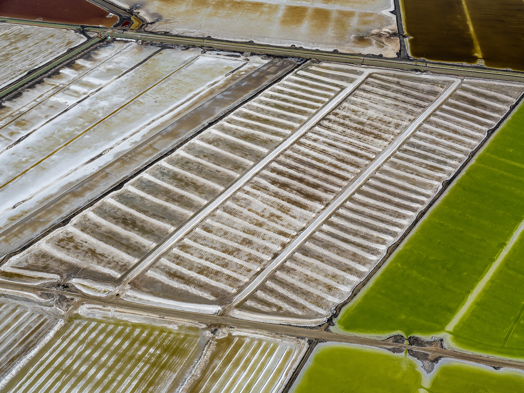 Aerial view of Compass Minerals solar evaporation ponds at the Great Salt Lake, showing geometric patterns of colorful mineral extraction ponds, levees, and industrial infrastructure impacting the lake's ecology.