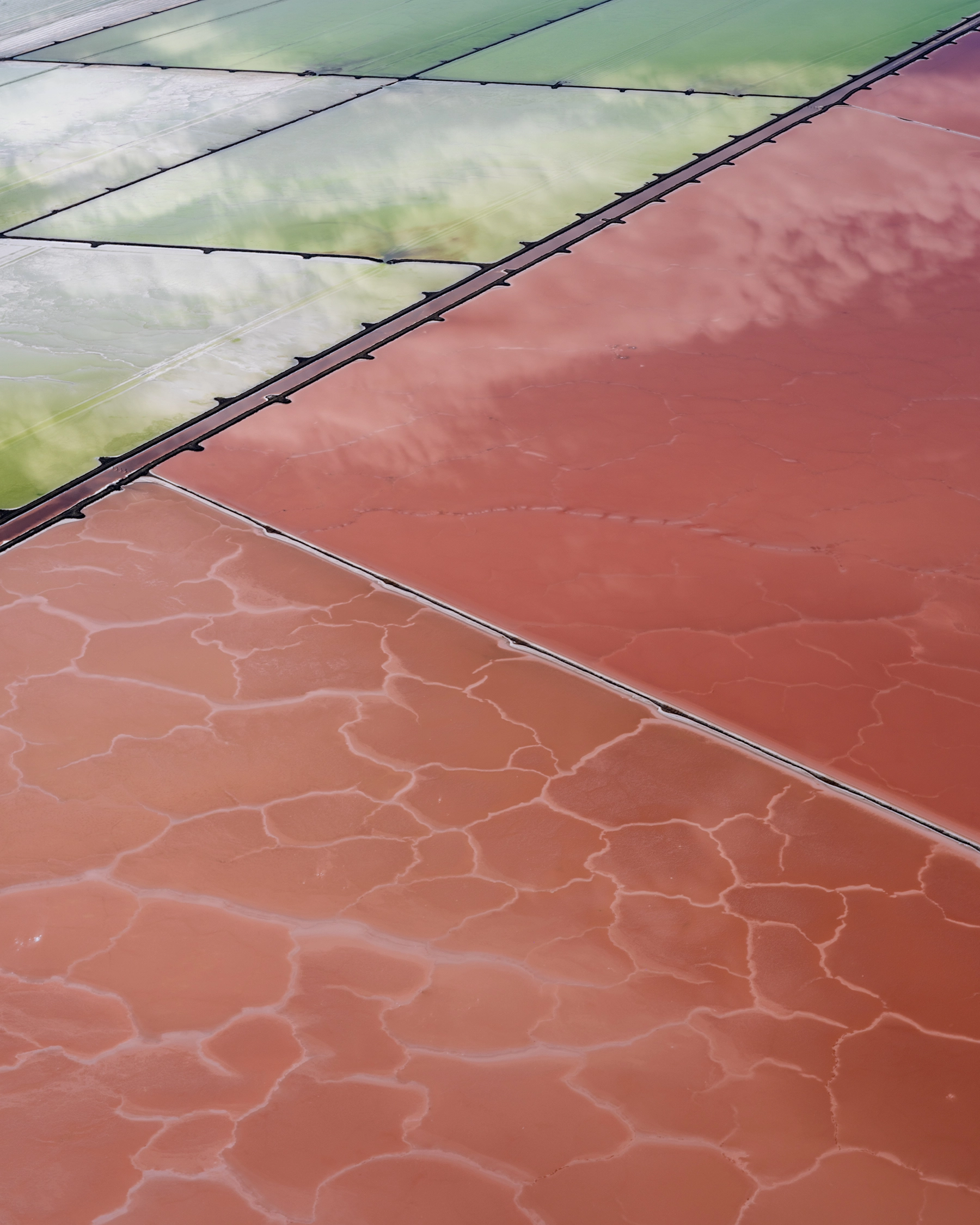 Aerial view of Compass Minerals solar evaporation ponds at the Great Salt Lake, showing geometric patterns of colorful mineral extraction ponds, levees, and industrial infrastructure impacting the lake's ecology.