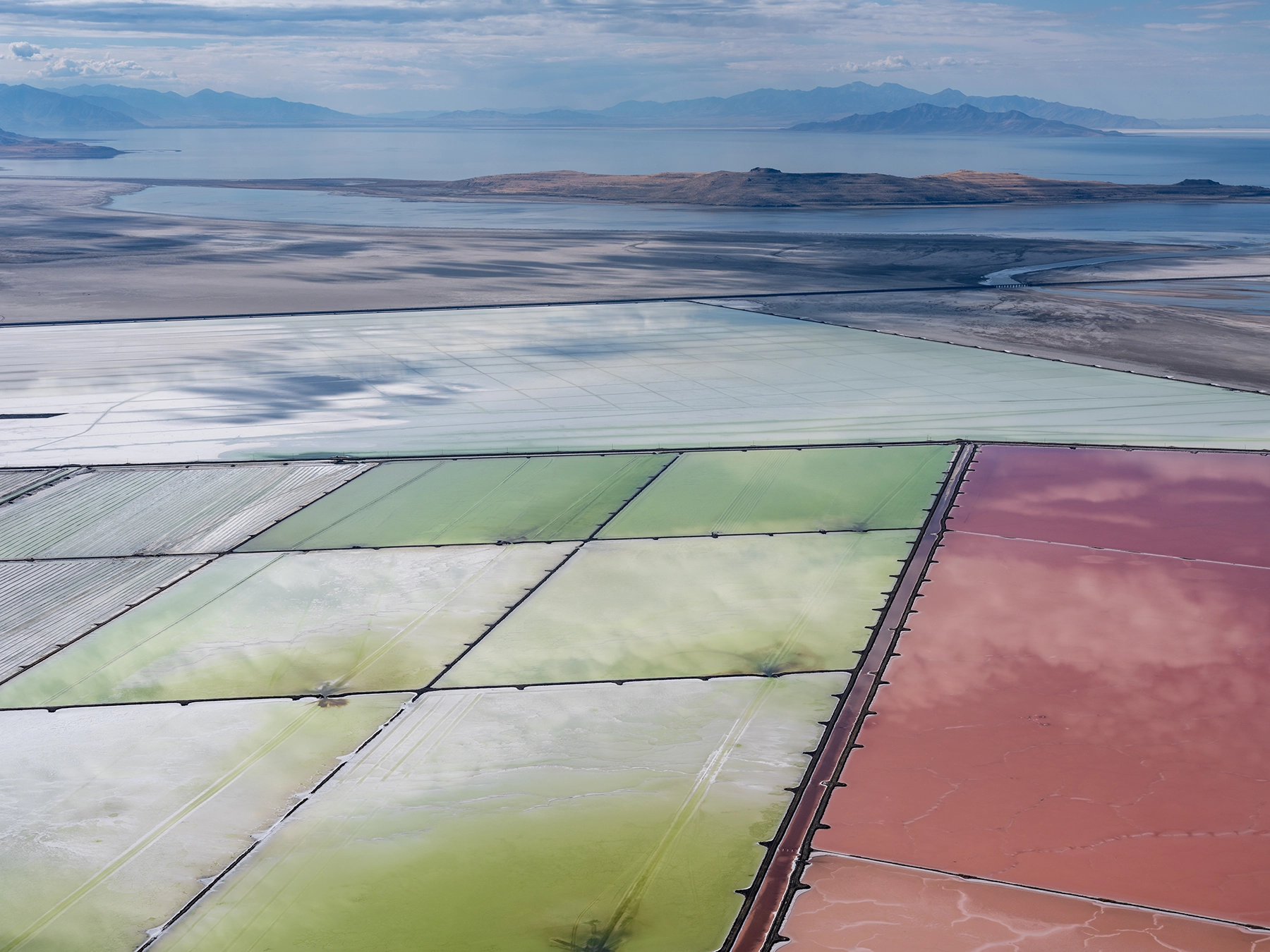 Aerial view of Compass Minerals solar evaporation ponds at the Great Salt Lake, showing geometric patterns of colorful mineral extraction ponds, levees, and industrial infrastructure impacting the lake's ecology.