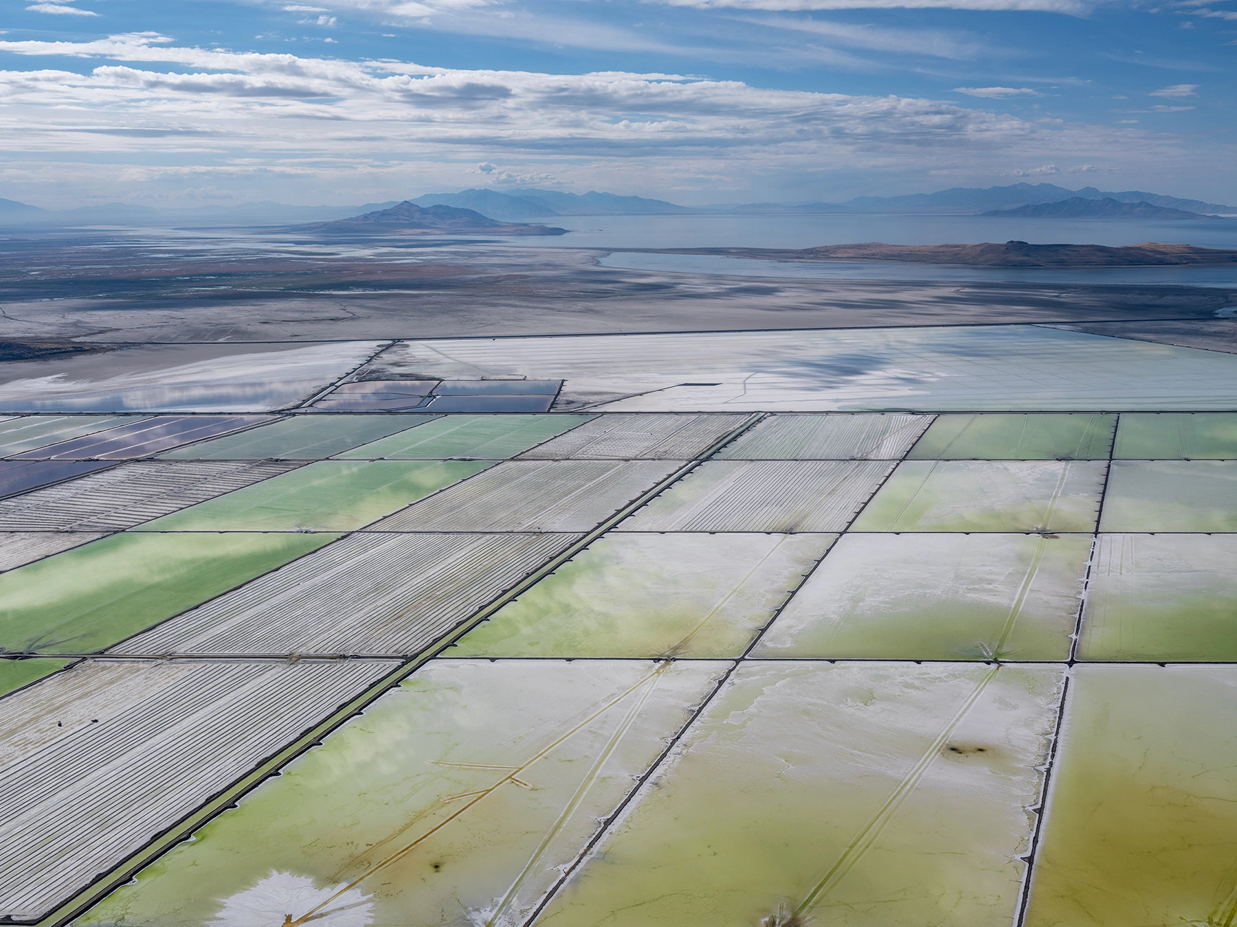 Aerial view of Compass Minerals solar evaporation ponds at the Great Salt Lake, showing geometric patterns of colorful mineral extraction ponds, levees, and industrial infrastructure impacting the lake's ecology.