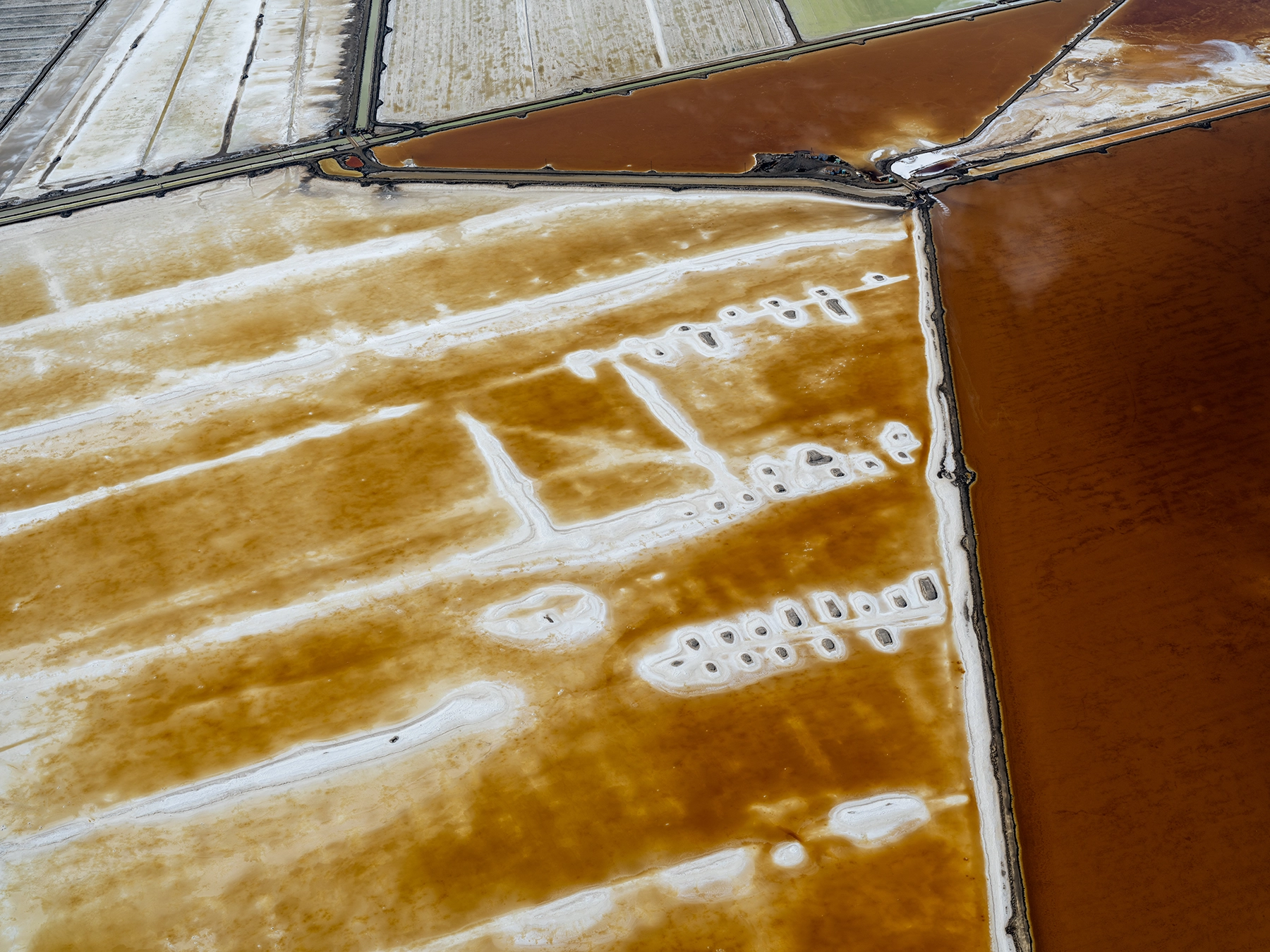 Aerial view of Compass Minerals solar evaporation ponds at the Great Salt Lake, showing geometric patterns of colorful mineral extraction ponds, levees, and industrial infrastructure impacting the lake's ecology.