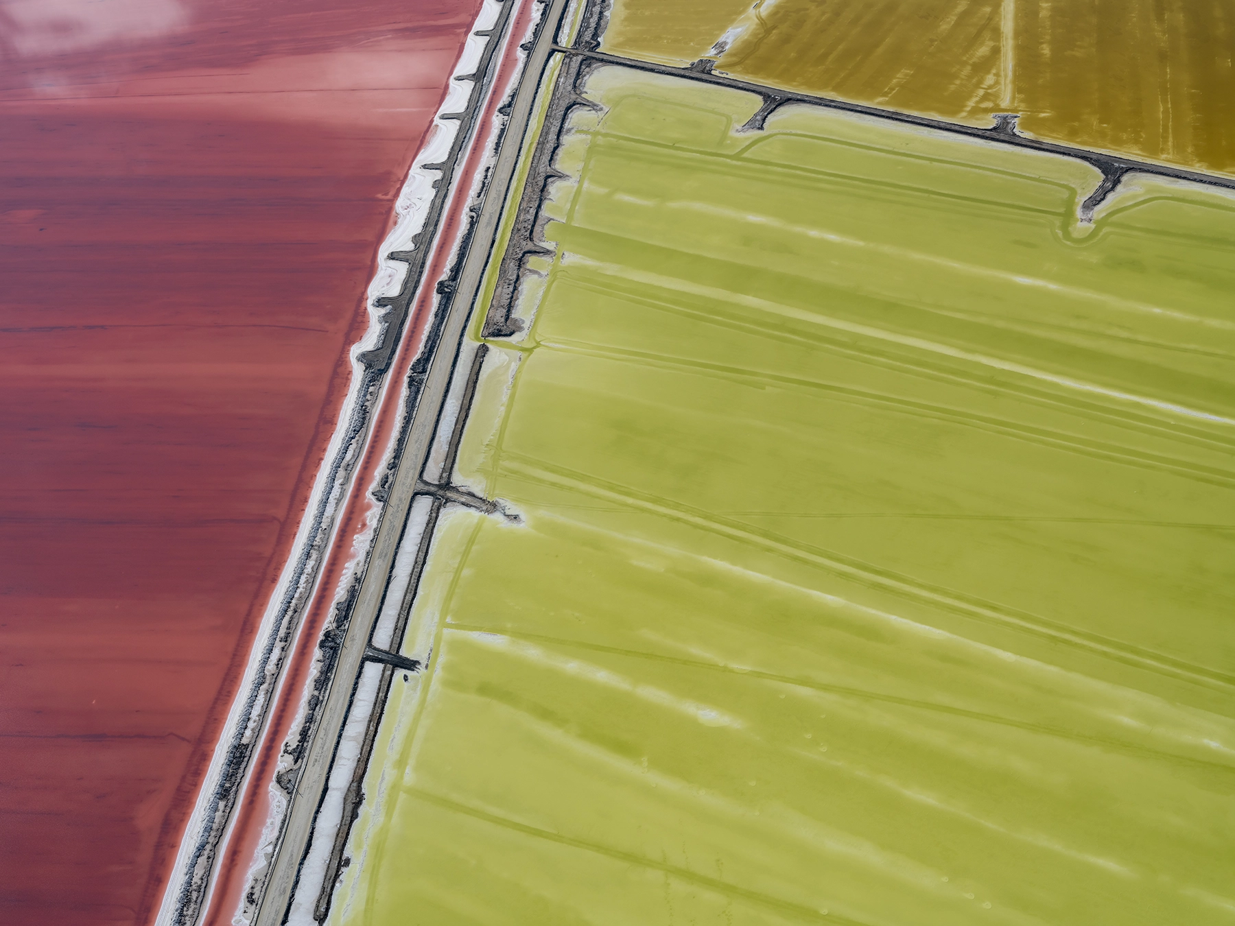Aerial view of Compass Minerals solar evaporation ponds at the Great Salt Lake, showing geometric patterns of colorful mineral extraction ponds, levees, and industrial infrastructure impacting the lake's ecology.