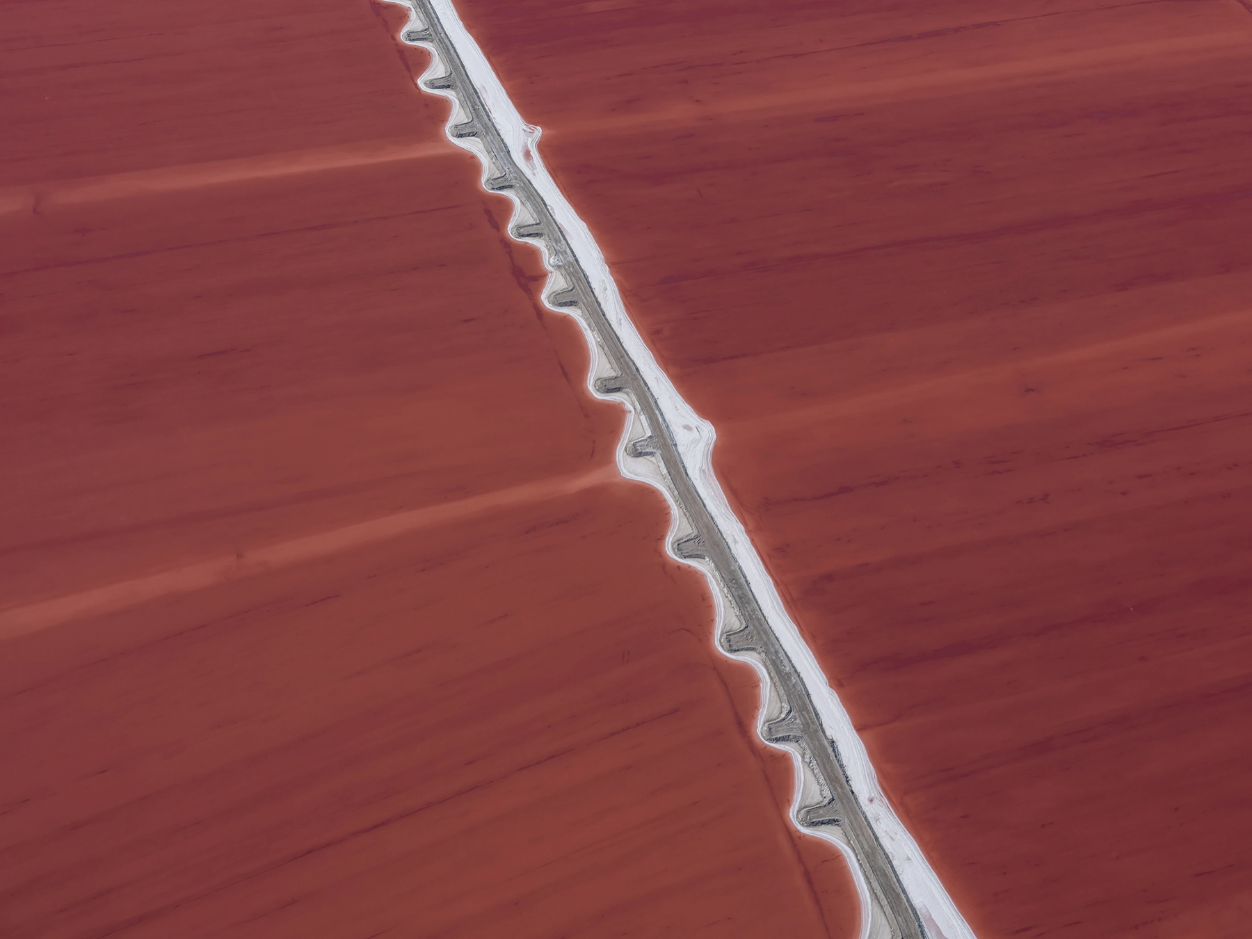 Aerial view of Compass Minerals solar evaporation ponds at the Great Salt Lake, showing geometric patterns of colorful mineral extraction ponds, levees, and industrial infrastructure impacting the lake's ecology.