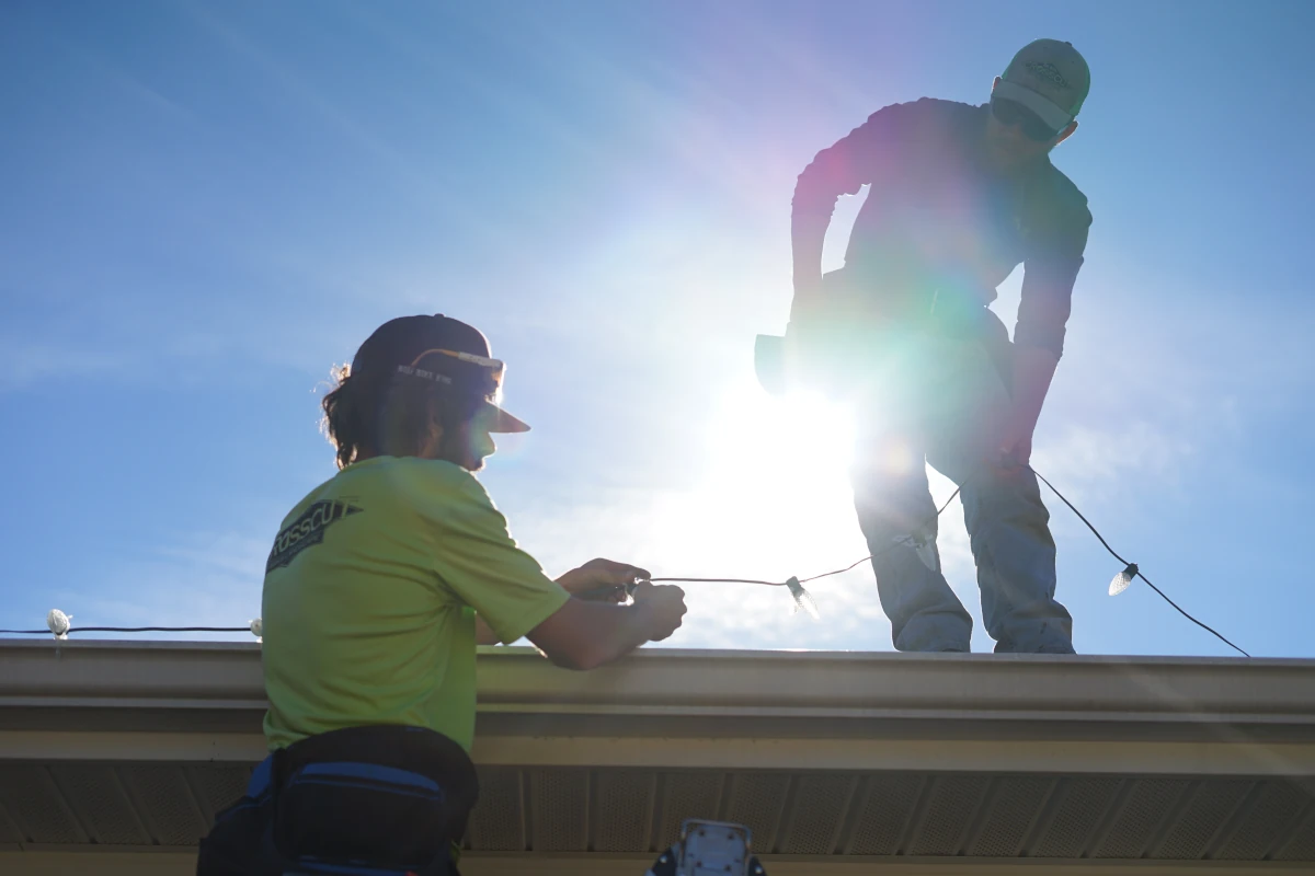 Two Cross cut employees installing Christmas lights on a roof.