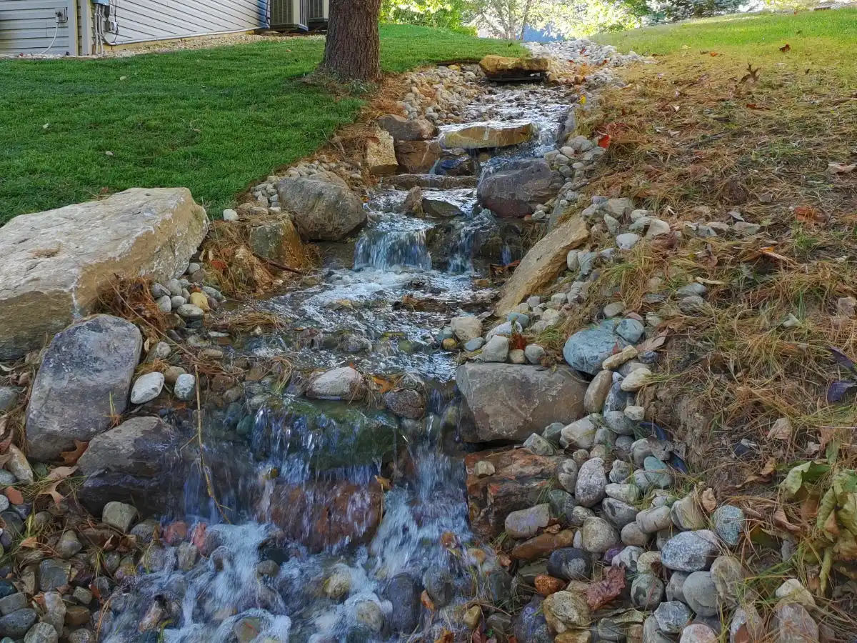 A beautiful drainage system with water flowing down like a stream in a residential backyard.