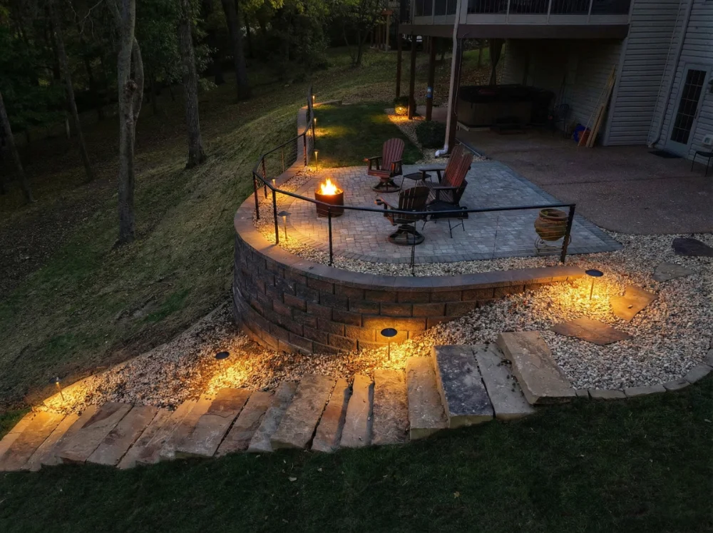 Outdoor patio with fire pit, Adirondack chairs, stone steps, and warm landscape lighting at dusk.