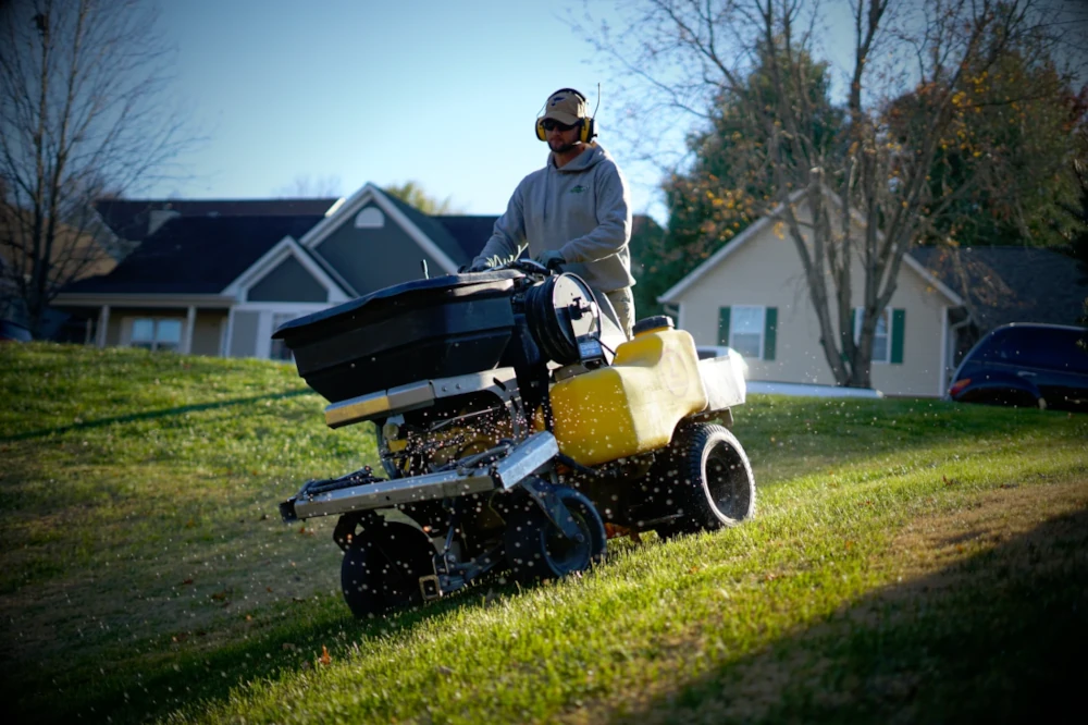 A Crosscut Employee operating a lawn fertilizing machine on a grassy slope in a residential neighborhood in Missouri