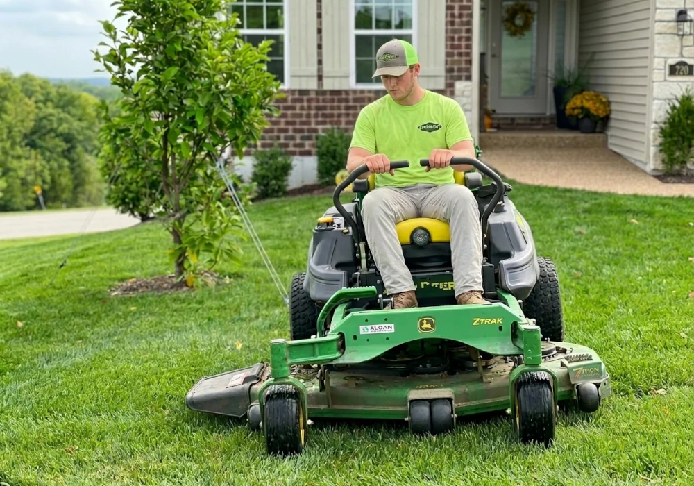 Crosscut employee mowing a lawn on a zero turn lawn mower.