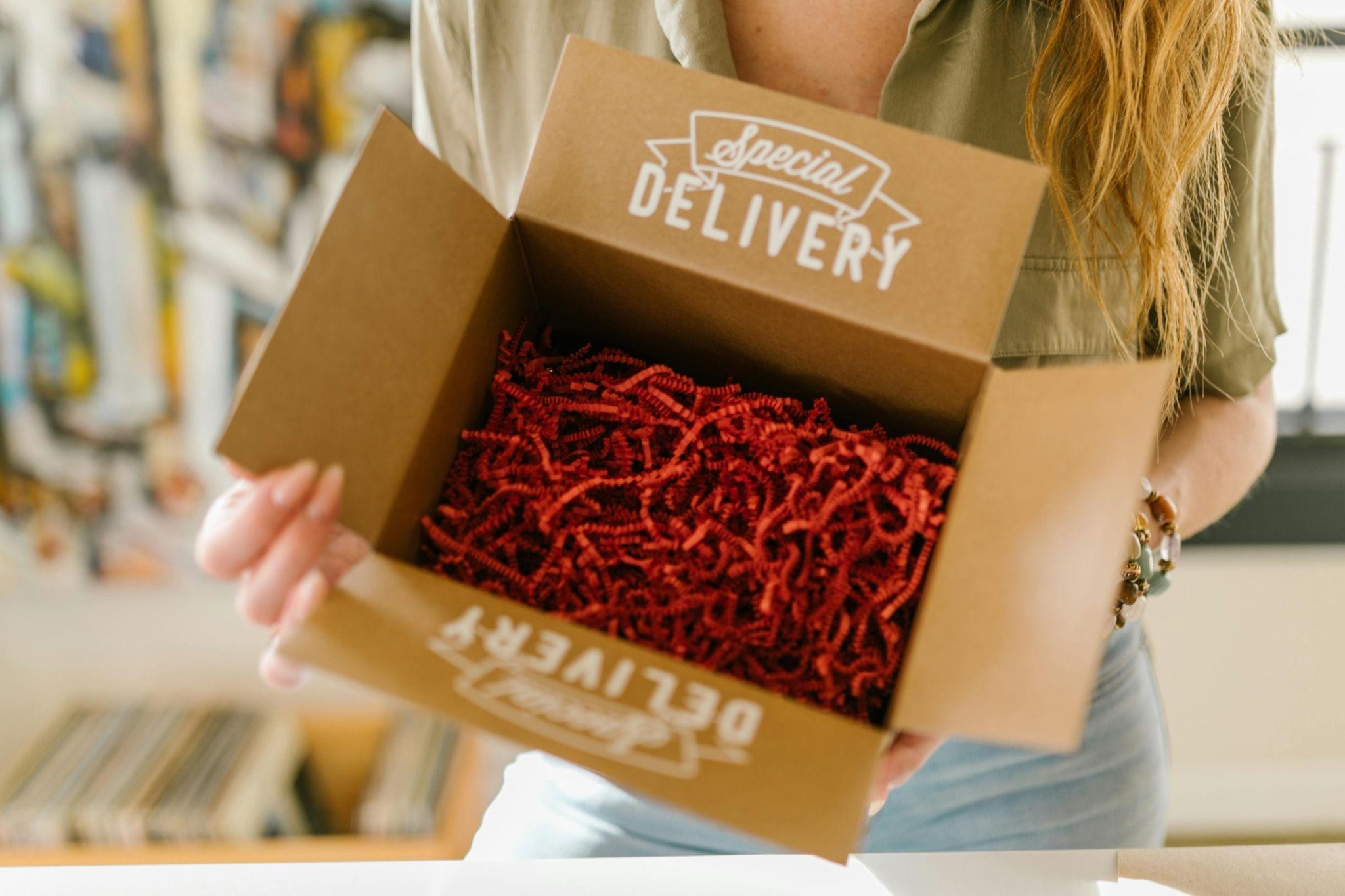 A person is holding an open box that contains red filler, and says, ‘Special Delivery’ on the top and bottom flaps of the box.