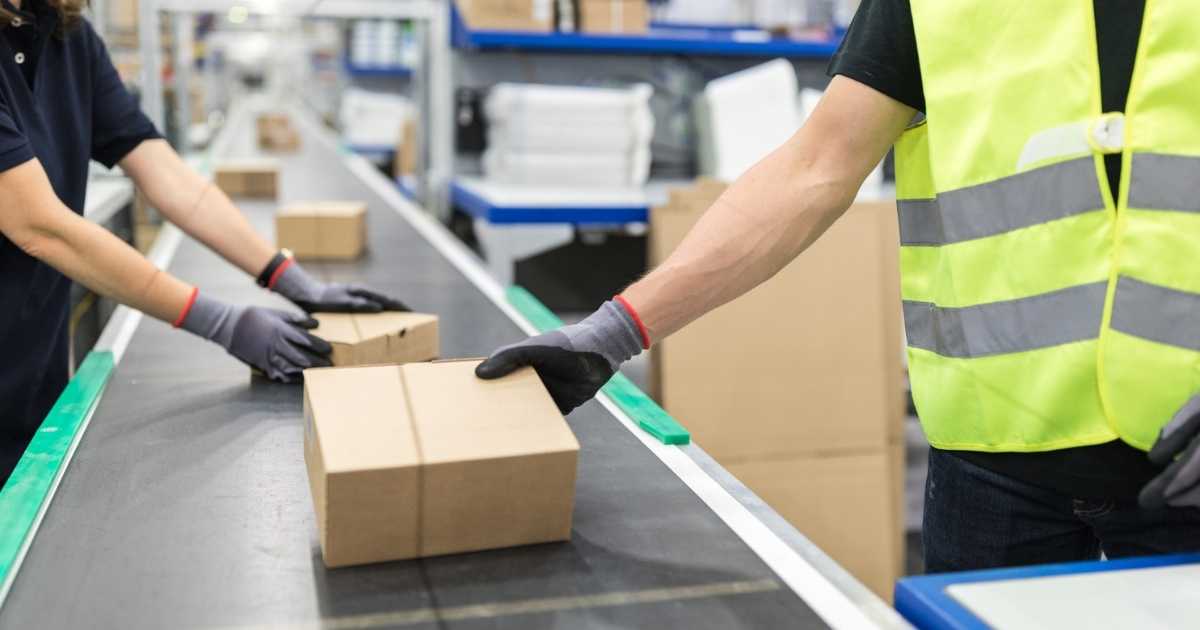 Warehouse workers removing boxes from a conveyor belt t obe shipped.