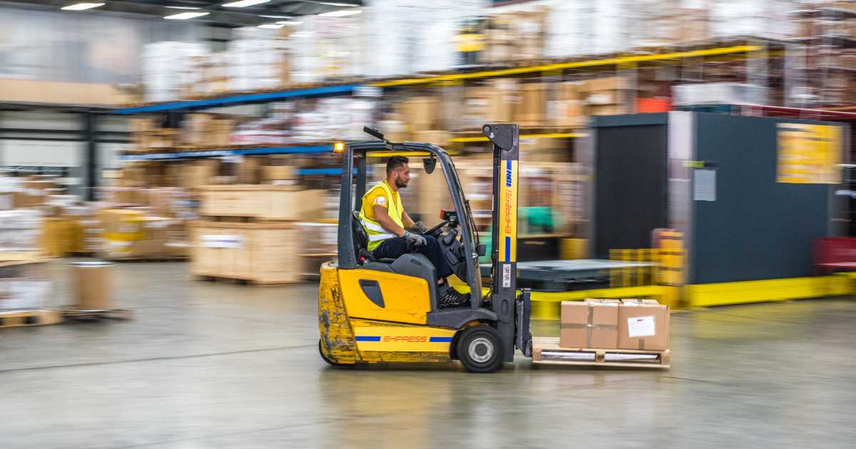 A picture of a warehouse worker driving a forklift with boxes on it.