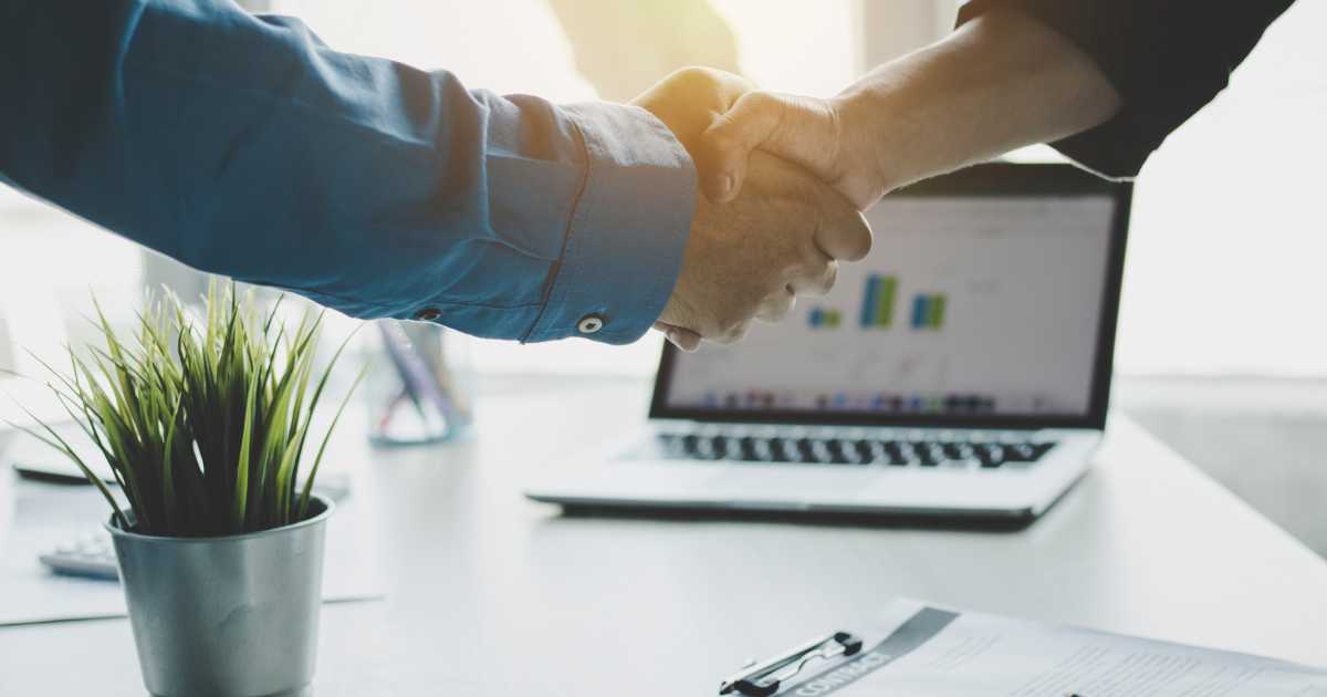 A picture of two people shaking hands in front of a laptop.