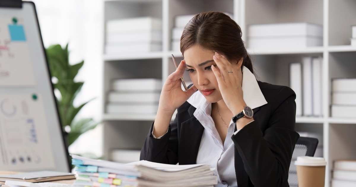 A picture of a frustrated worker holding her hands to her head.