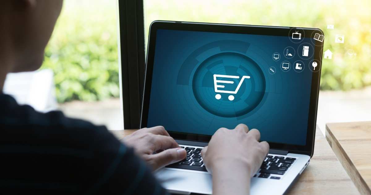 A picture of a person using a laptop with a shopping cart on the screen denoting ecommerce sales.