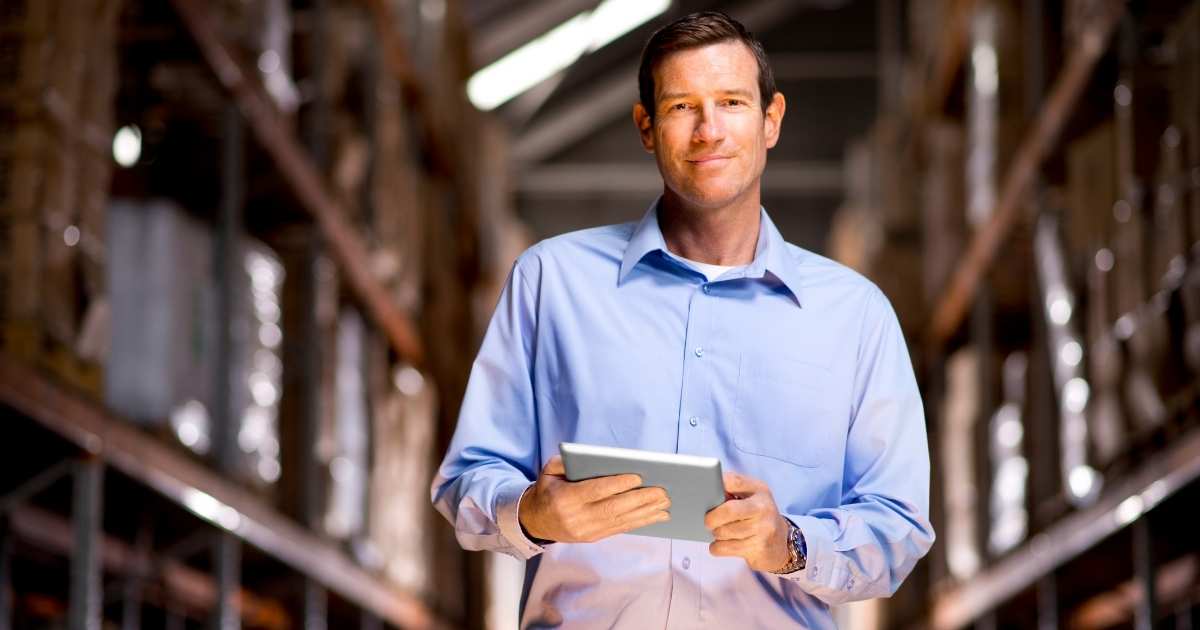 A picture of a happy warehouse worked in a button down working on a tablet. 