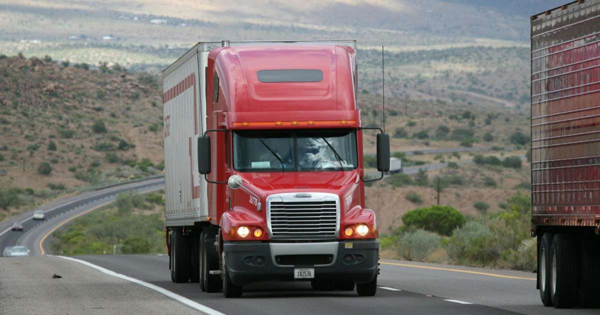 A red semi-truck is driving on a highway.