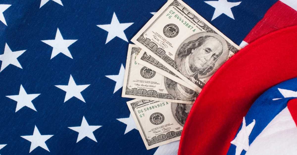 A picture of the American flag with four 100 dollar bills lying on it.