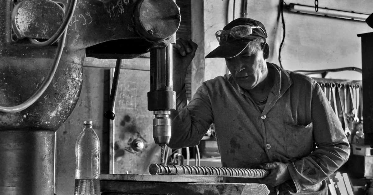 A black and white picture of an older worker operating a punch press machine.