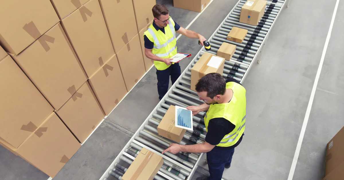 Two warehouse workers reviewing packages on a conveyor belt.