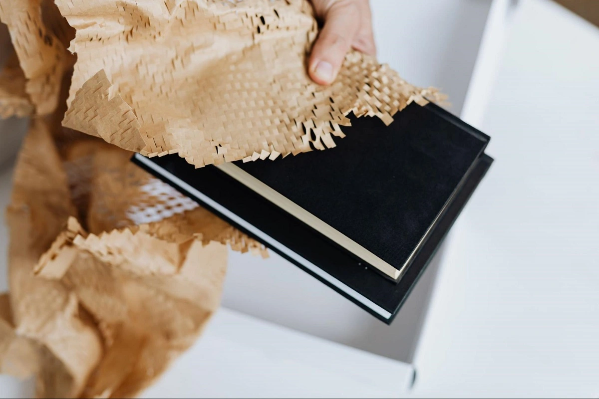 A hand is holding two black books partially covered with honeycomb paper.