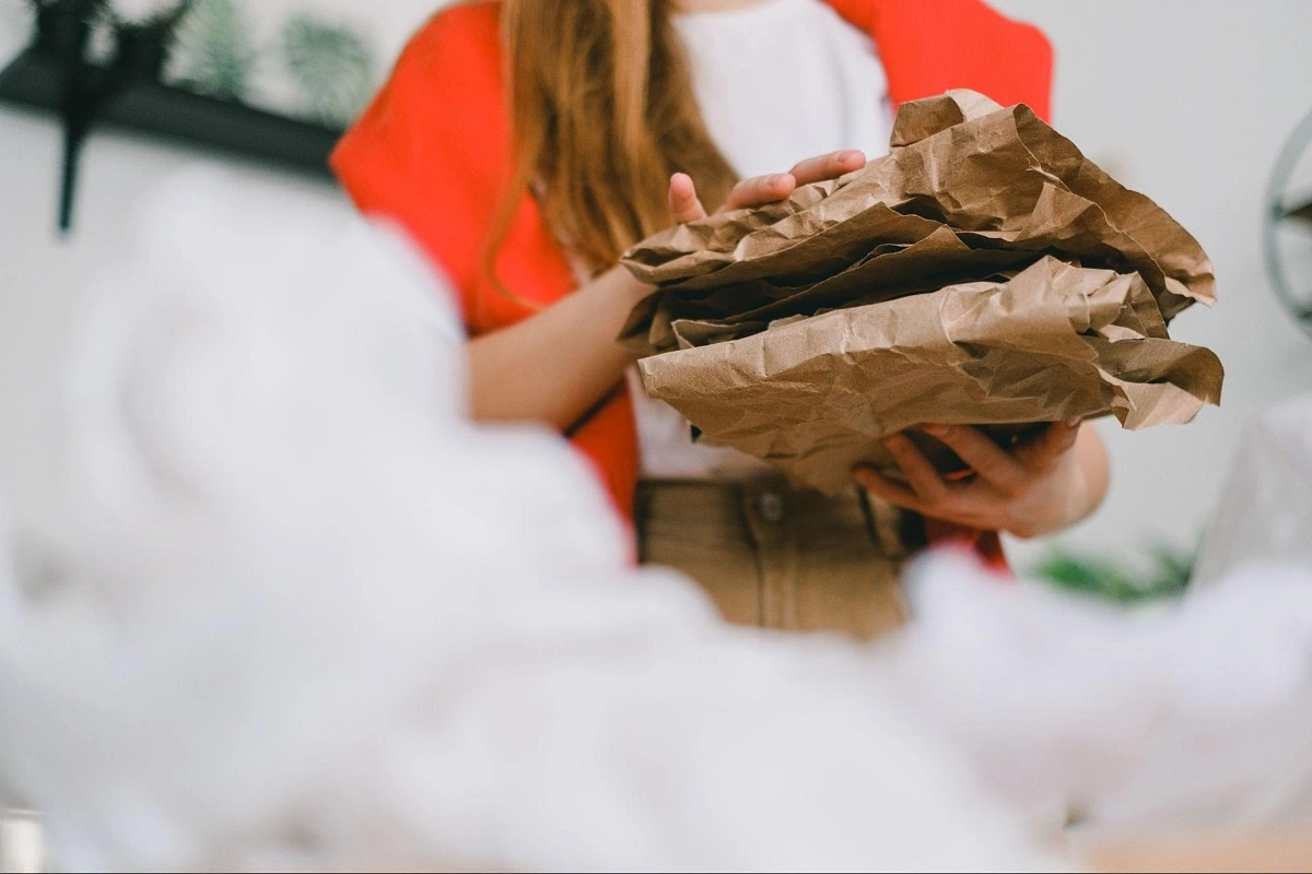 A person holding a crumpled stack of brown packing paper.