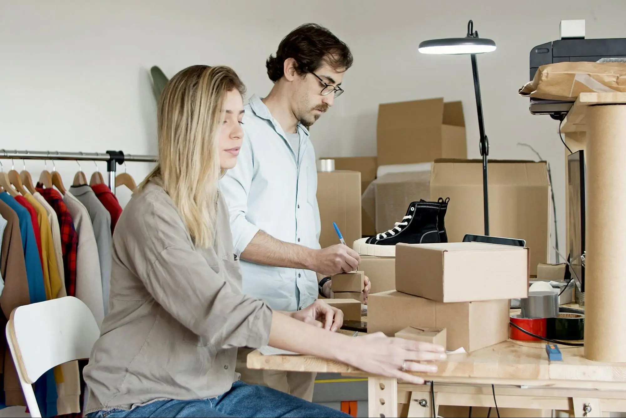Two people are preparing packages in a small home business, one writing on the boxes and the other sorting them.