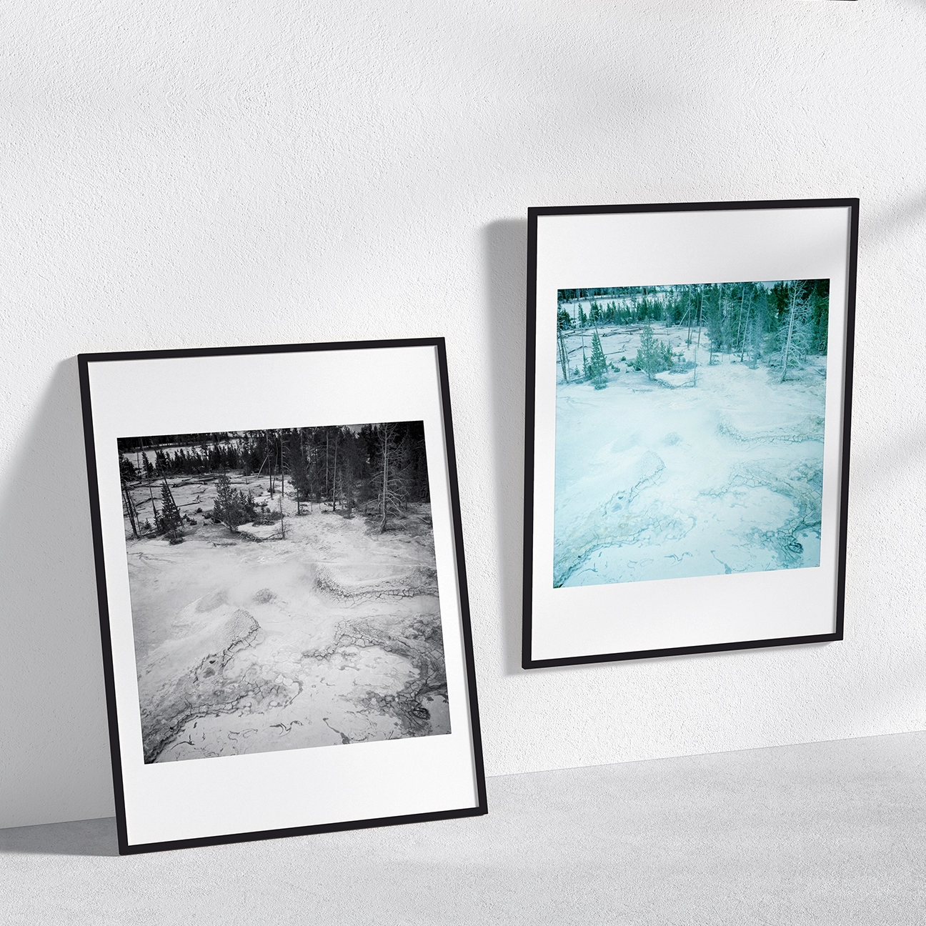 Wall mockup showing two framed versions of “Sulphur Pit, Yellowstone”—one black-and-white and one color—featuring pale geothermal ground, mineral textures, and a line of trees in the distance.