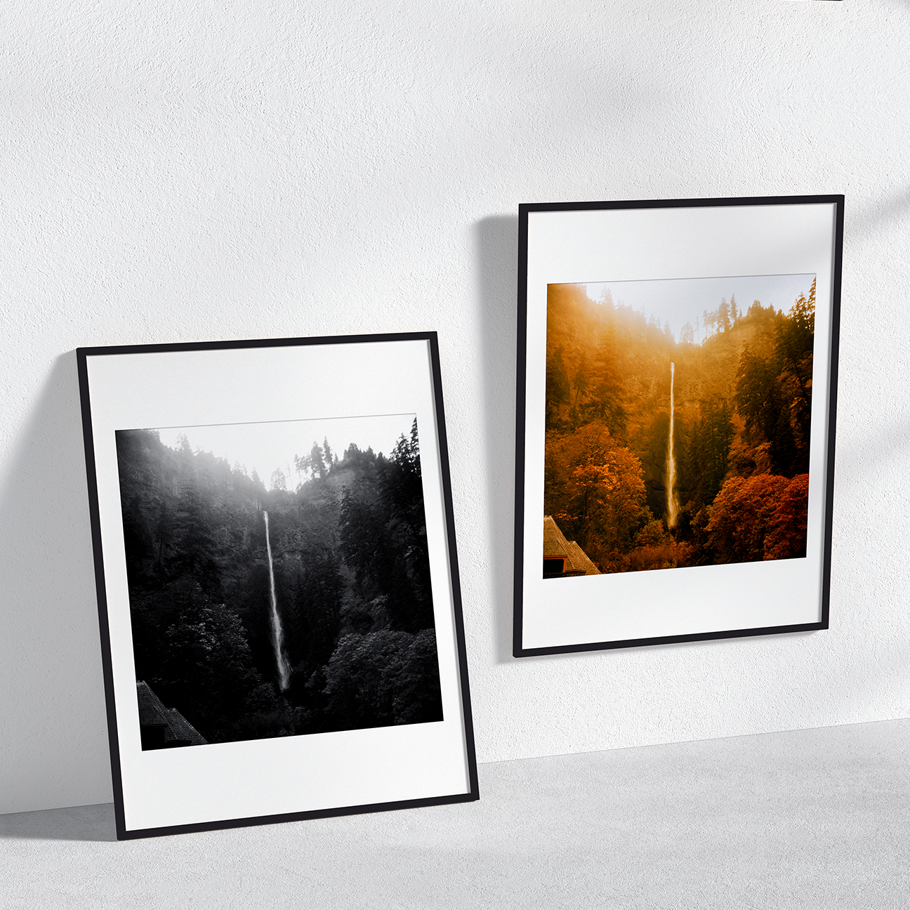 Wall mockup with two framed versions of “Multnomah Falls Autumn, Oregon”: a black-and-white print leaning against the wall and a color version beside it, capturing the tall waterfall framed by sunlit golden trees and mist rising through the forest.