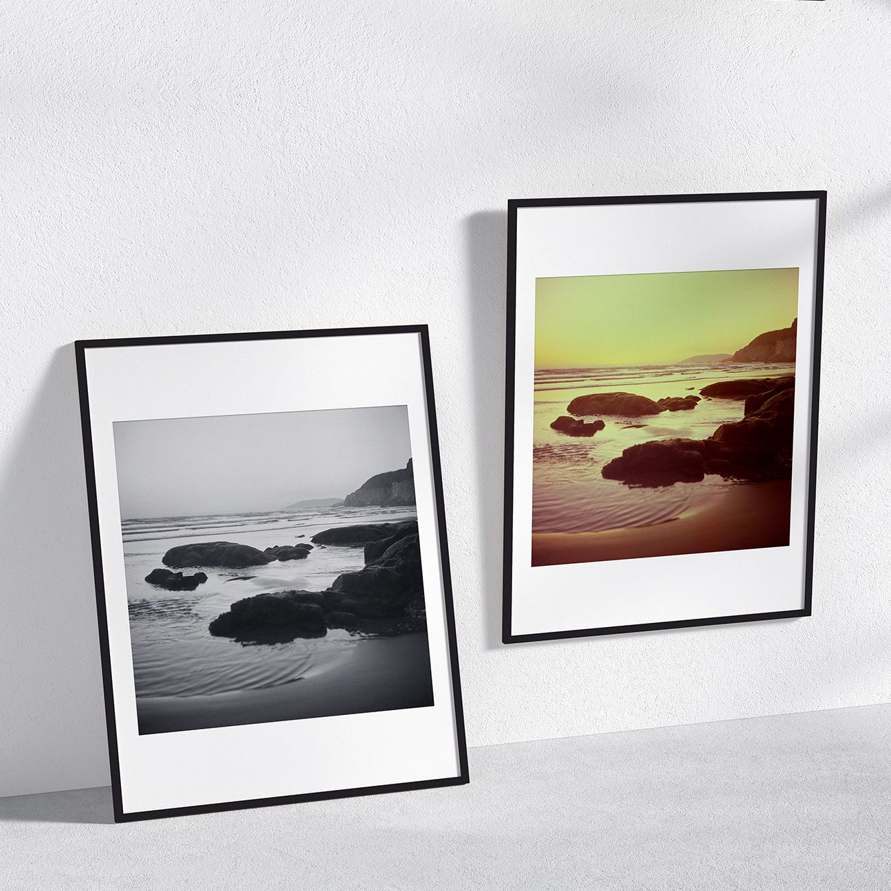 Alt in-room mockup featuring two framed “Pismo Beach Rocks Sunset” photo prints side by side: a black-and-white shoreline scene and a warm, golden sunset version with tide-washed rocks, gentle surf, and a distant coastal bluff.