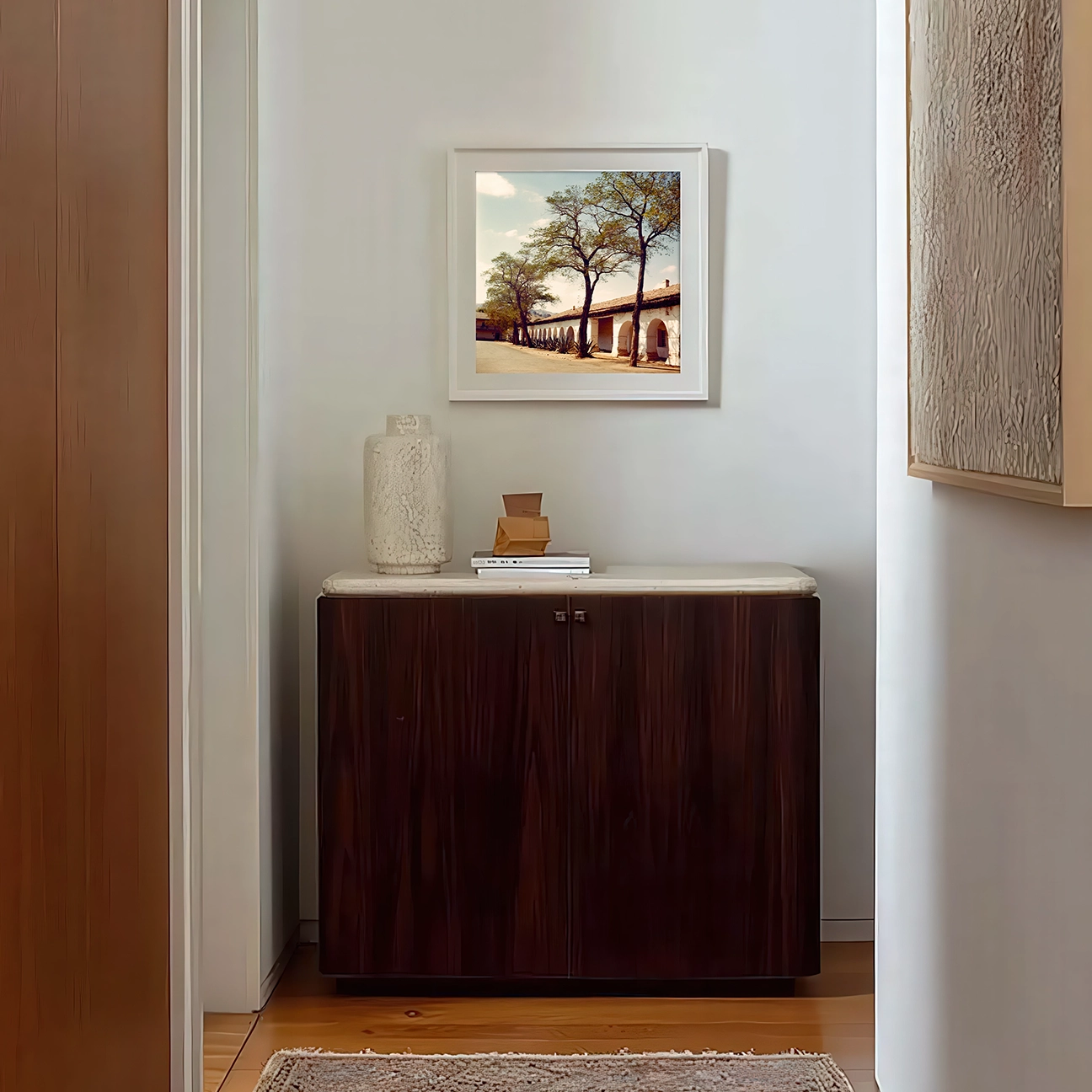 Analog photograph of Mission San Juan Bautista, sunlight on arches and trees, styled above a dark wood console for warm California charm.