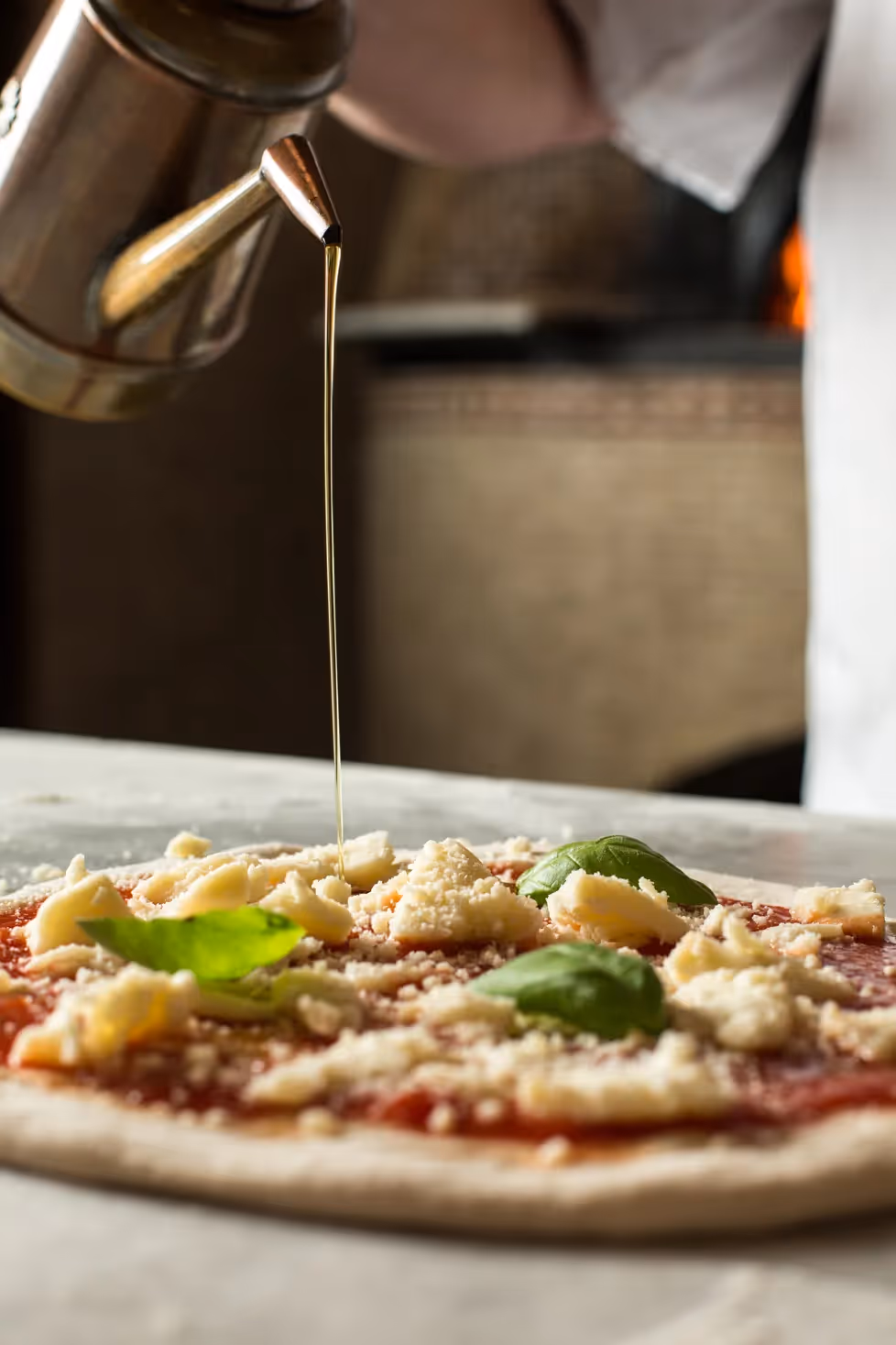Chef at Il Pizzaiolo drizzling olive oil on a pizza