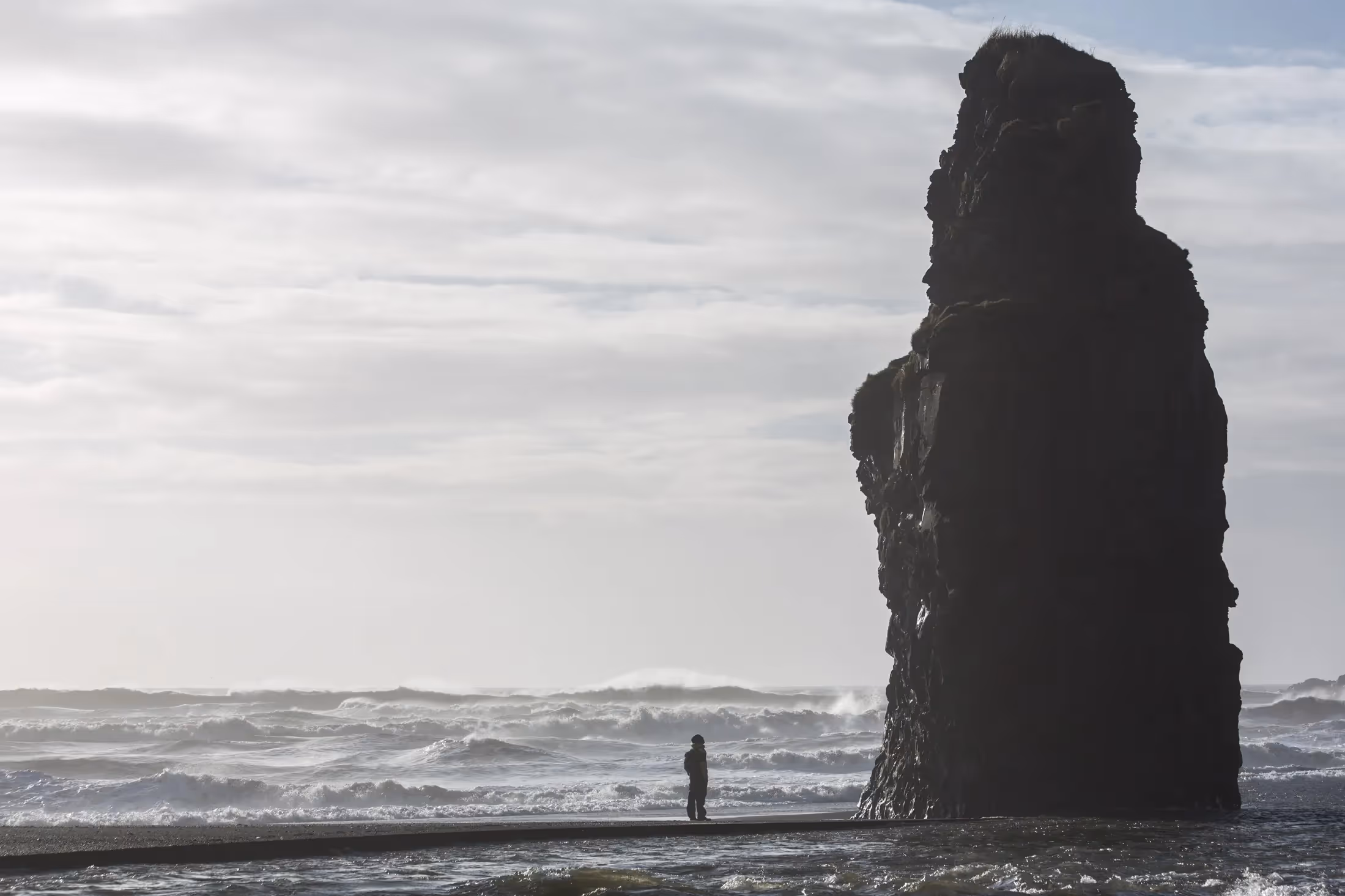 Person standing on a beach next to a large rock formation in Iceland