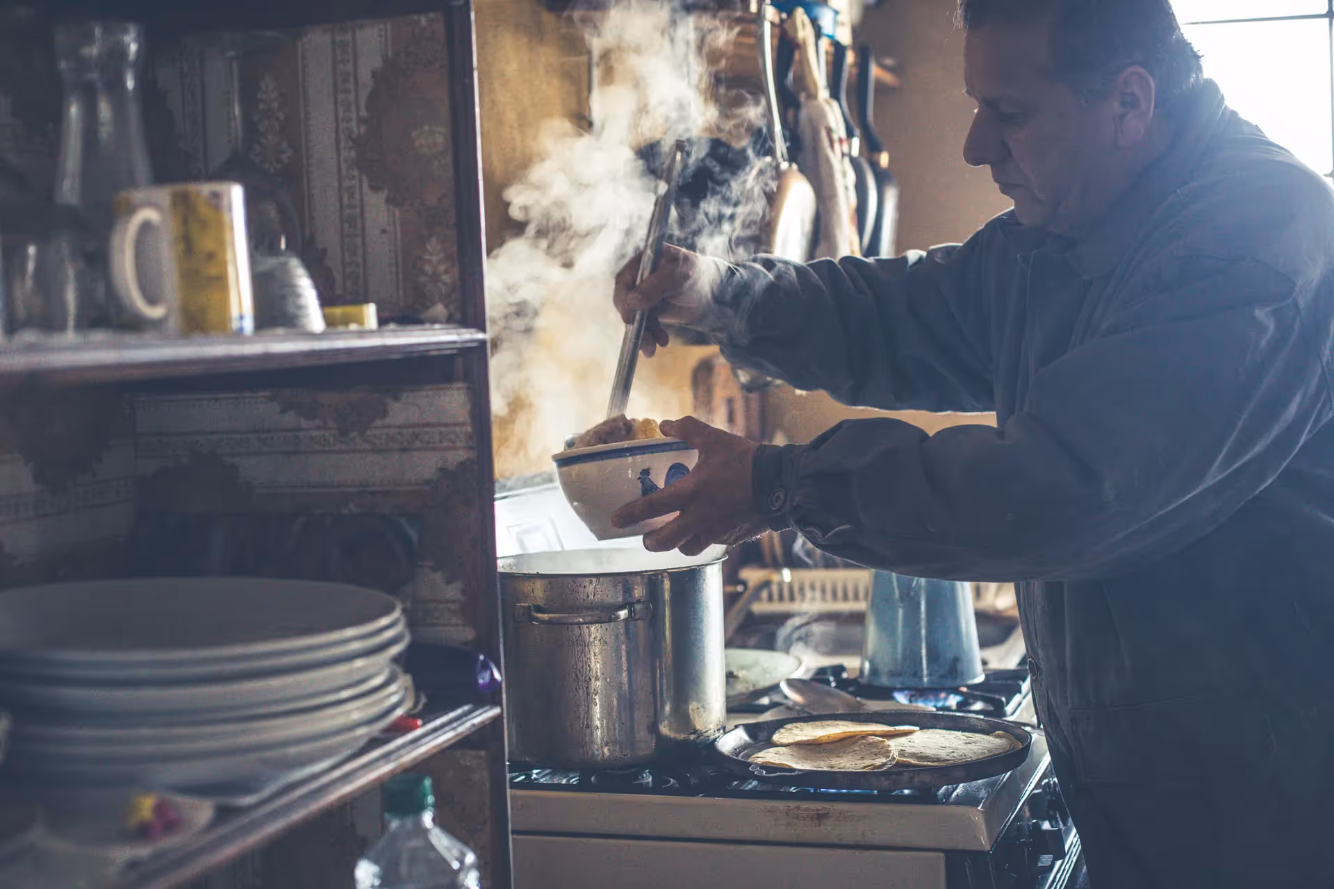 Man in rustic kitchen pouring soup into a bowl