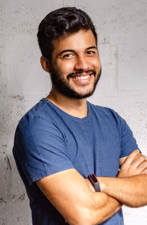 A smiling man with his arms crossed in front of a white wall.