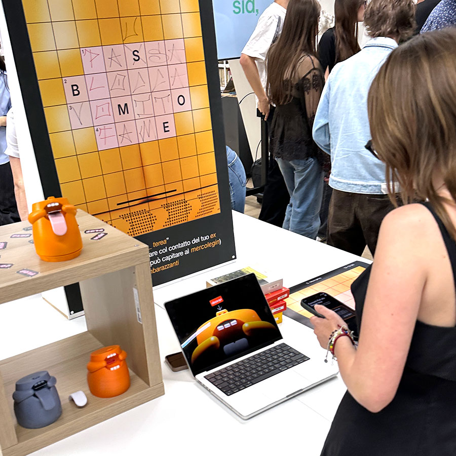 Studentessa esplora un gioco interattivo con dispositivi fisici arancioni, una griglia grafica e un'interfaccia digitale durante la mostra SID.