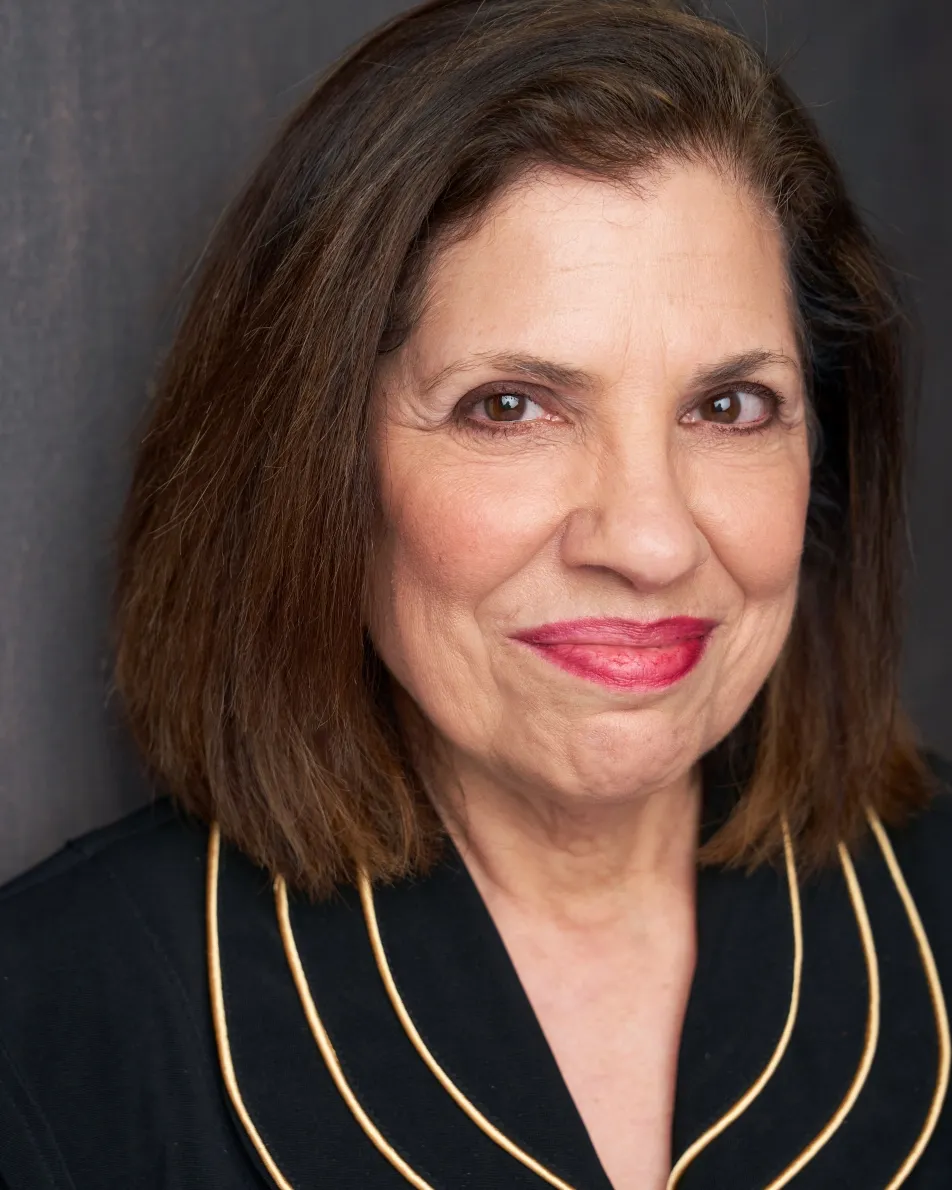 Atlanta theatrical actor headshot — mature female actor with short brown hair, confident smile in black top with gold trim, authority and matriarch role type.