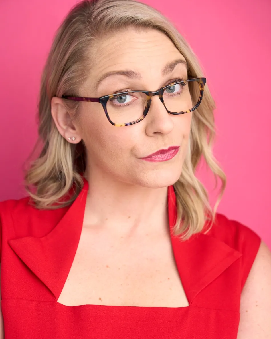 Atlanta commercial actor headshot — blonde female actor with glasses, red top, sarcastic expression against bright pink background, character-driven style.