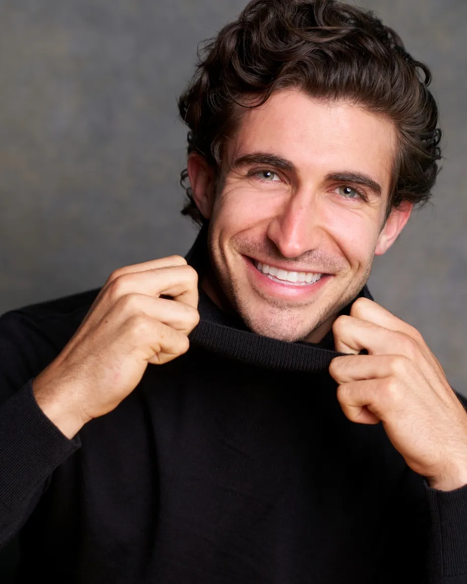 Atlanta commercial actor headshot — male actor with curly dark hair, bright toothy smile, playful pose in black sweater, studio background.