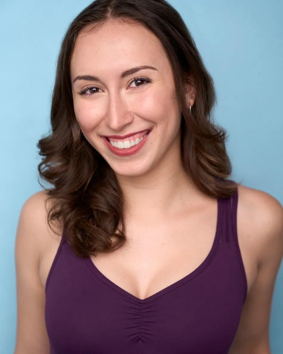 Atlanta commercial / musical theater headshot — young female theater actress with bright toothy smile, purple top, light blue background.
