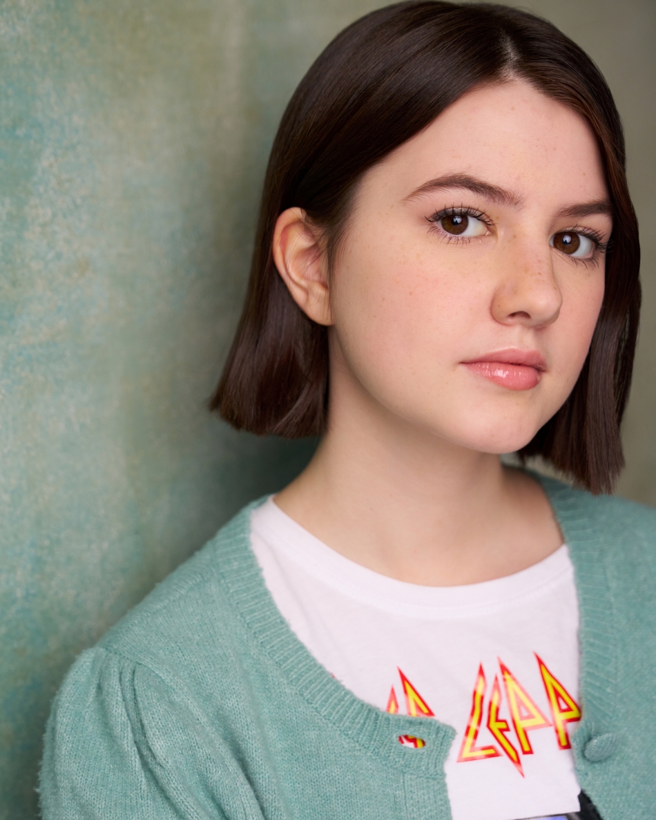 Atlanta theatrical actor headshot — teen female actor with straight dark hair, thoughtful expression in green cardigan and Def Leppard tee, dramatic young adult casting look.