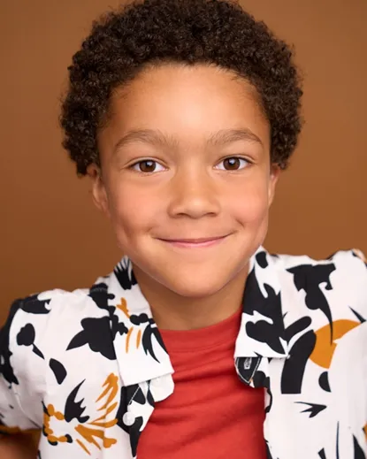 Atlanta actor headshot — young boy with curly hair, warm smile in patterned shirt against brown background, welcoming image for contact page.