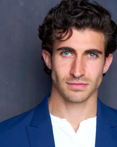 Virginia D.C. theatrical actor headshot — young male actor with curly dark hair, serious confident expression in blue blazer and white shirt, professional dramatic look.