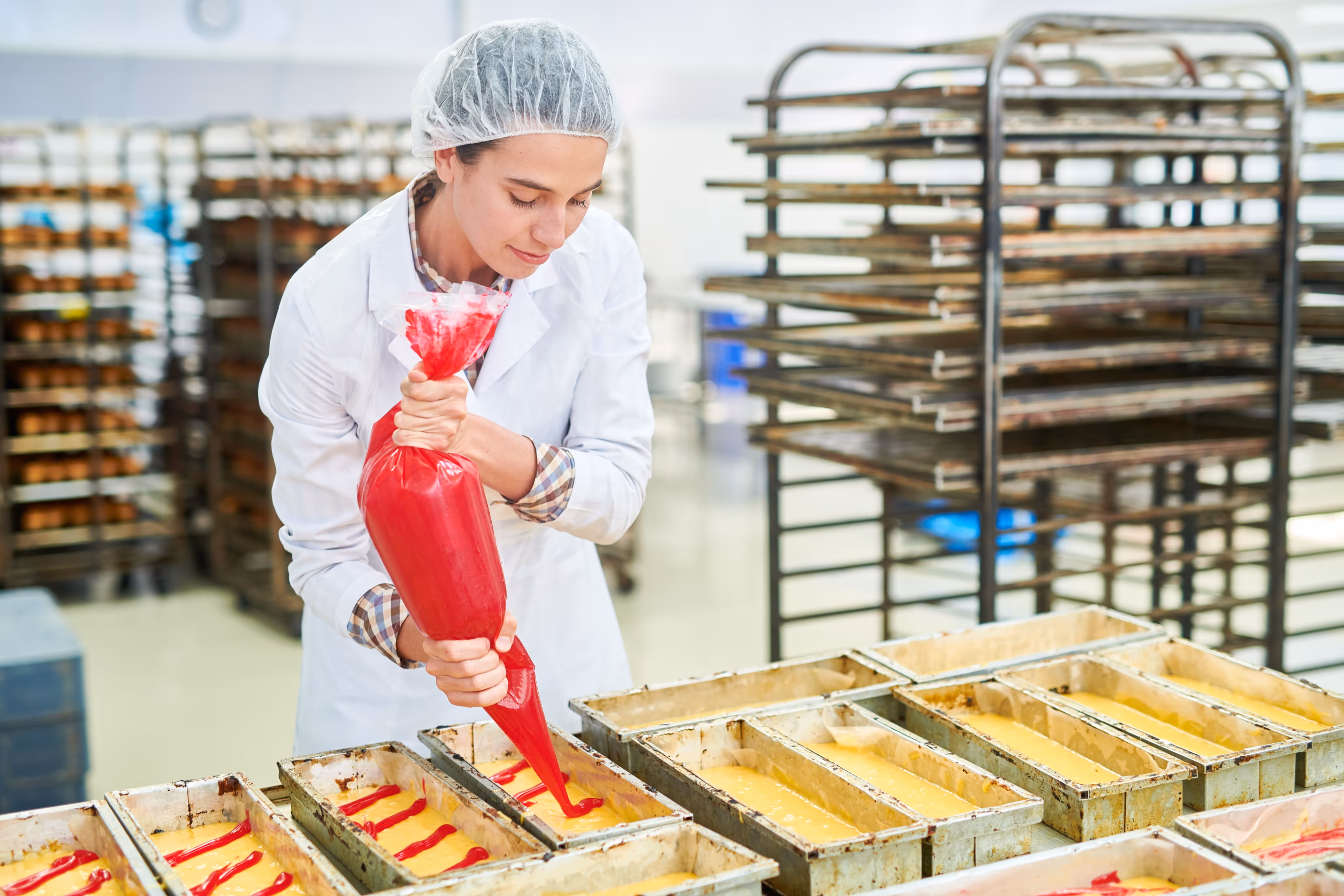A food production worker at a confectionary factory piping into a cake pan